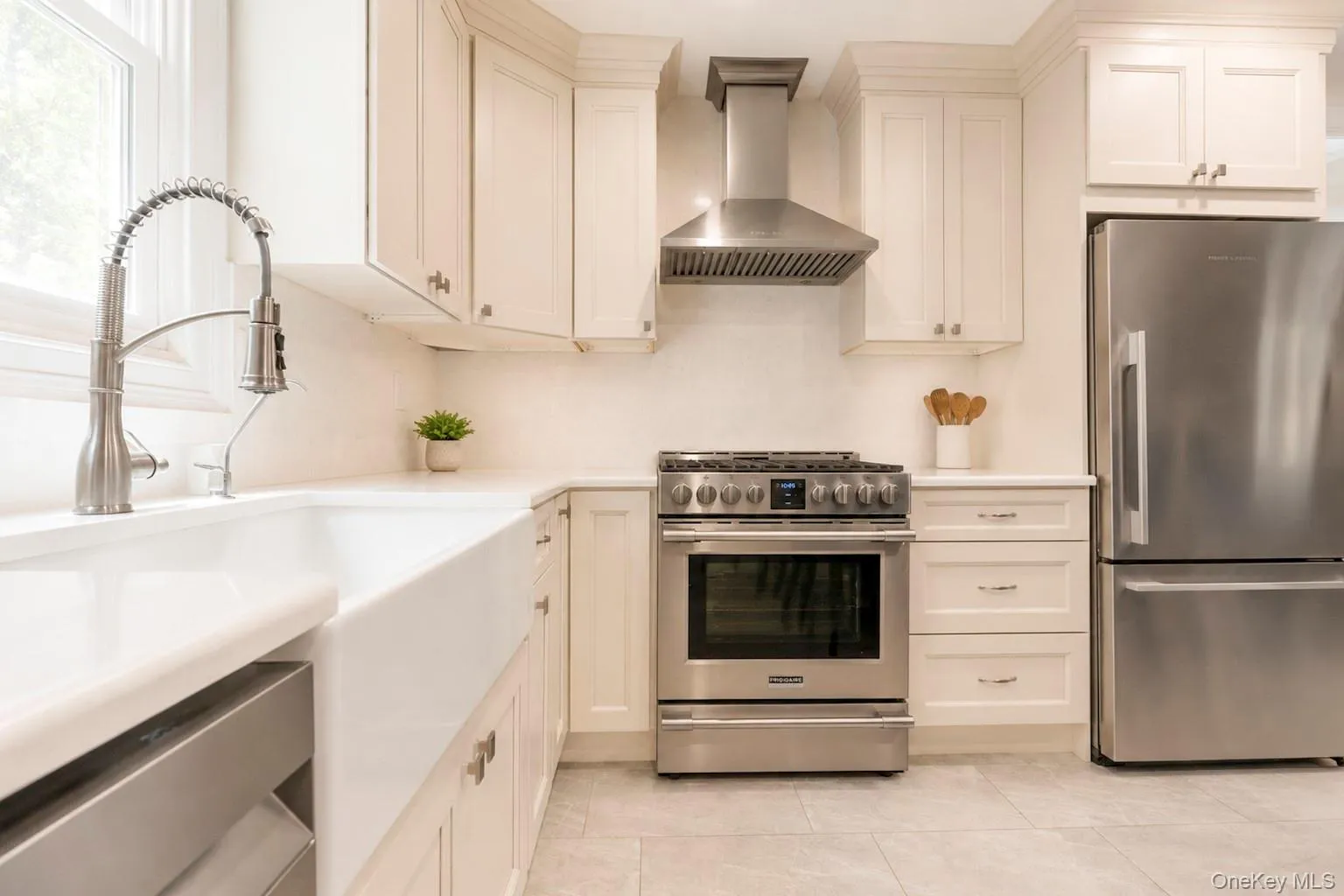 Kitchen featuring a farmhouse sink with a gooseneck faucet, light-toned cabinetry, stainless steel appliances, and tile flooring Kitchen featuring a farmhouse sink with a gooseneck faucet, light-toned cabinetry, stainless steel appliances, and tile flooring