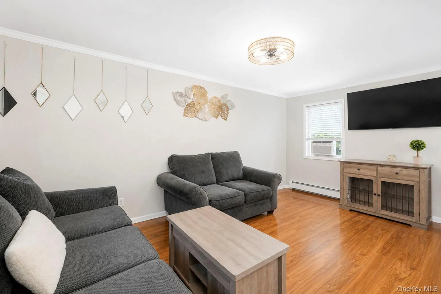 Spacious living area featuring wood-finish flooring, light neutral wall tones, and crown molding Spacious living area featuring wood-finish flooring, light neutral wall tones, and crown molding