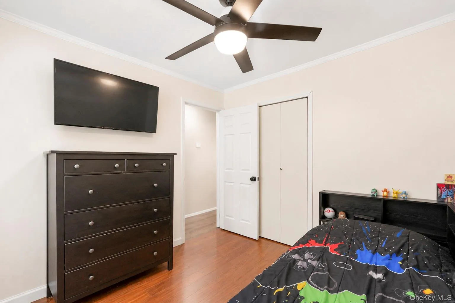 Bedroom featuring wood-finish flooring, a ceiling fan with integrated lighting, and a built-in closet with bifold doors Bedroom featuring wood-finish flooring, a ceiling fan with integrated lighting, and a built-in closet with bifold doors