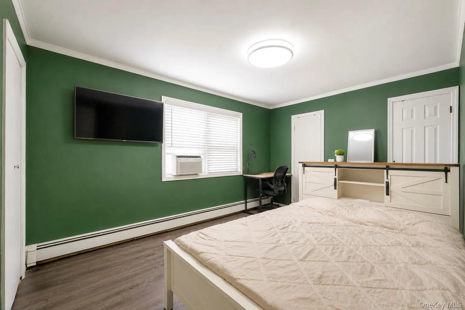 Green-painted room featuring wood-finish flooring, white baseboards, and a window with blinds Green-painted room featuring wood-finish flooring, white baseboards, and a window with blinds