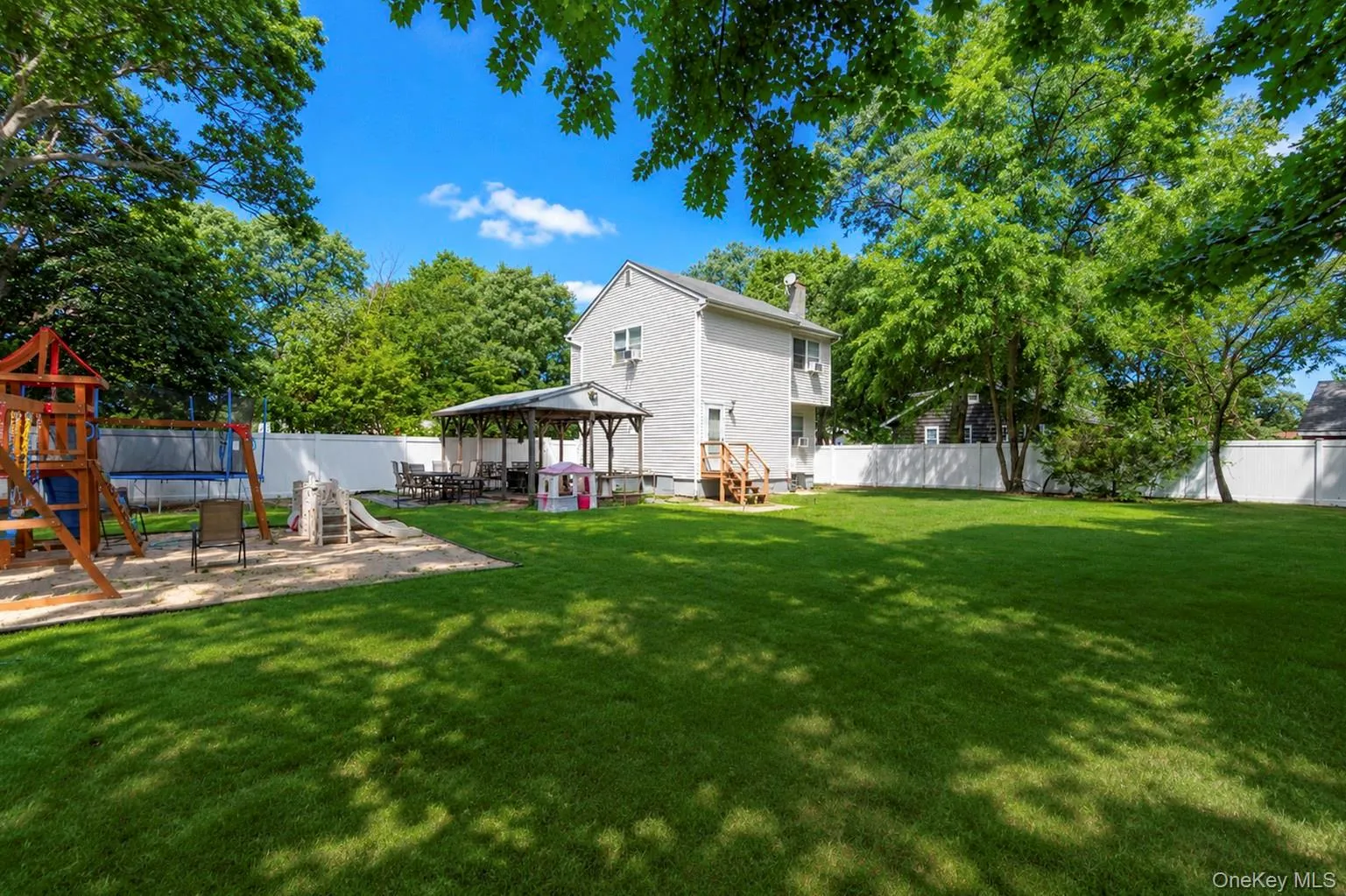 Expansive green lawn with mature trees and a white privacy fence Expansive green lawn with mature trees and a white privacy fence