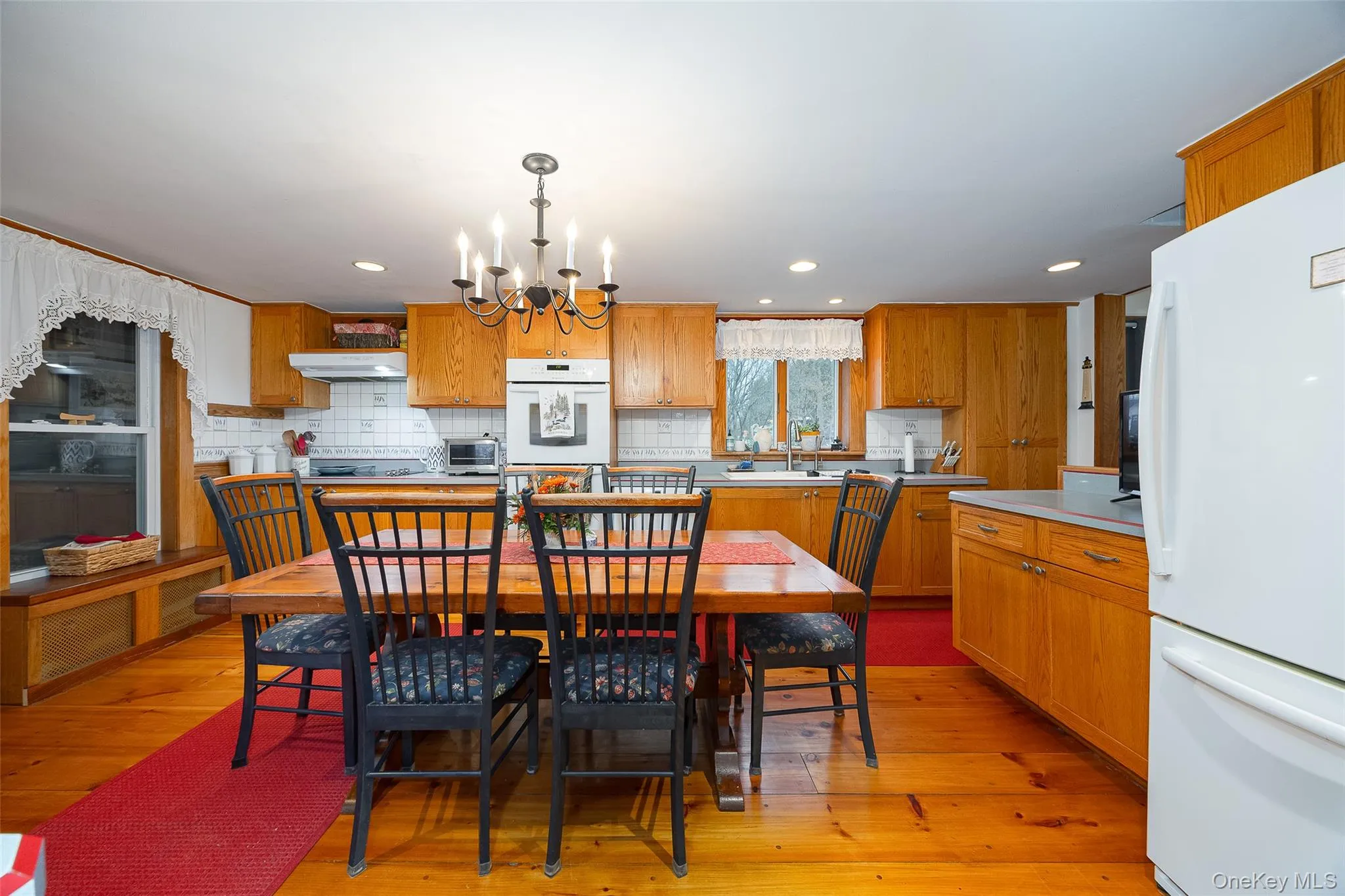 Kitchen featuring light countertops, freestanding refrigerator, a chandelier, brown cabinetry, and pendant lighting Kitchen featuring light countertops, freestanding refrigerator, a chandelier, brown cabinetry, and pendant lighting