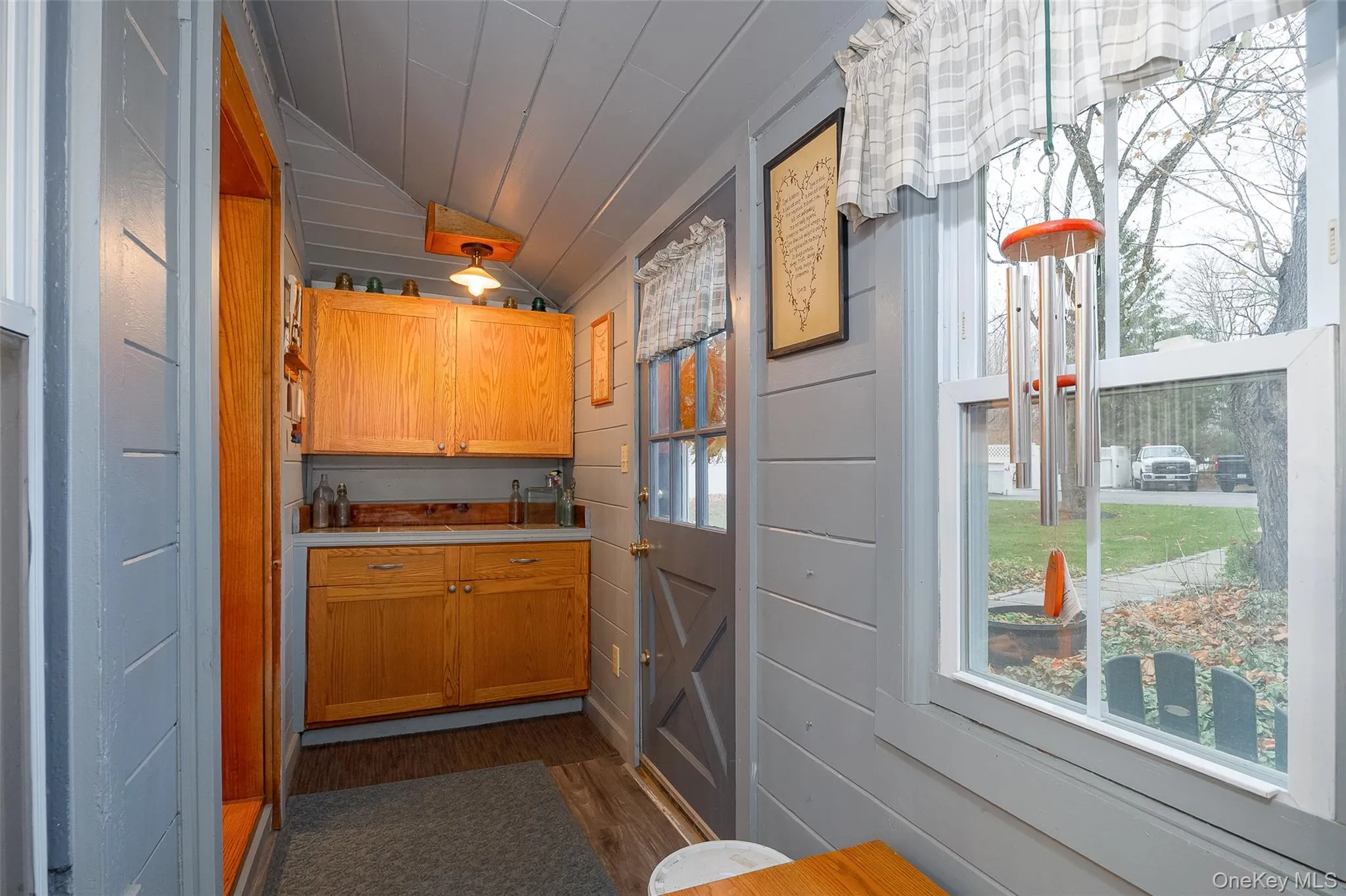 Entry featuring lofted ceiling, light countertops, wooden walls, and brown cabinetry Entry featuring lofted ceiling, light countertops, wooden walls, and brown cabinetry