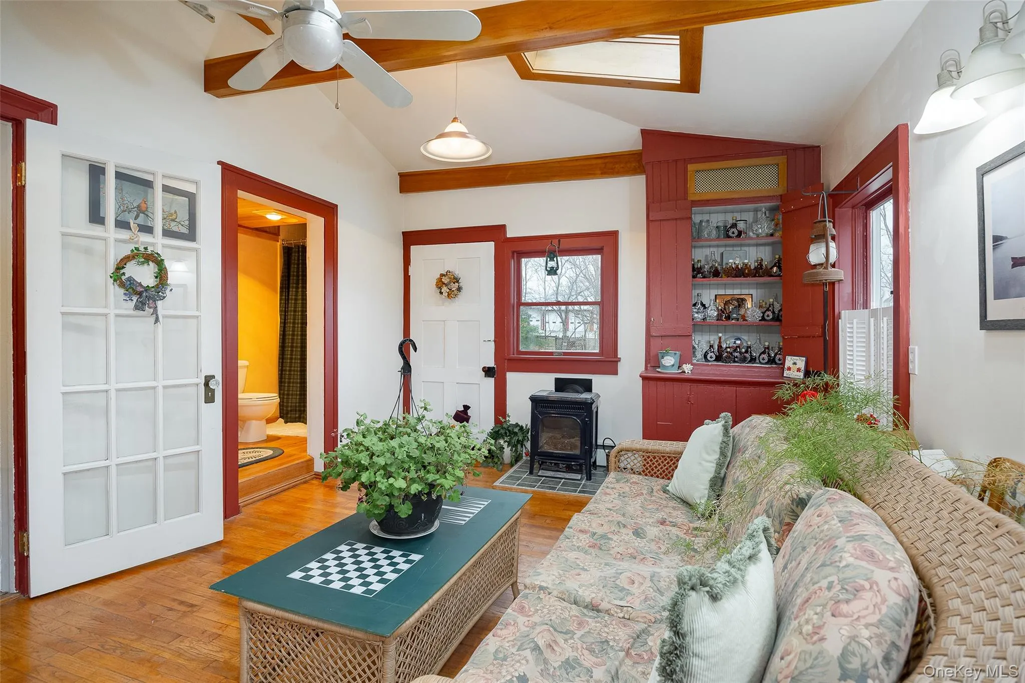 Living room featuring lofted ceiling, a wood stove, light wood-type flooring, ceiling fan, and a skylight Living room featuring lofted ceiling, a wood stove, light wood-type flooring, ceiling fan, and a skylight