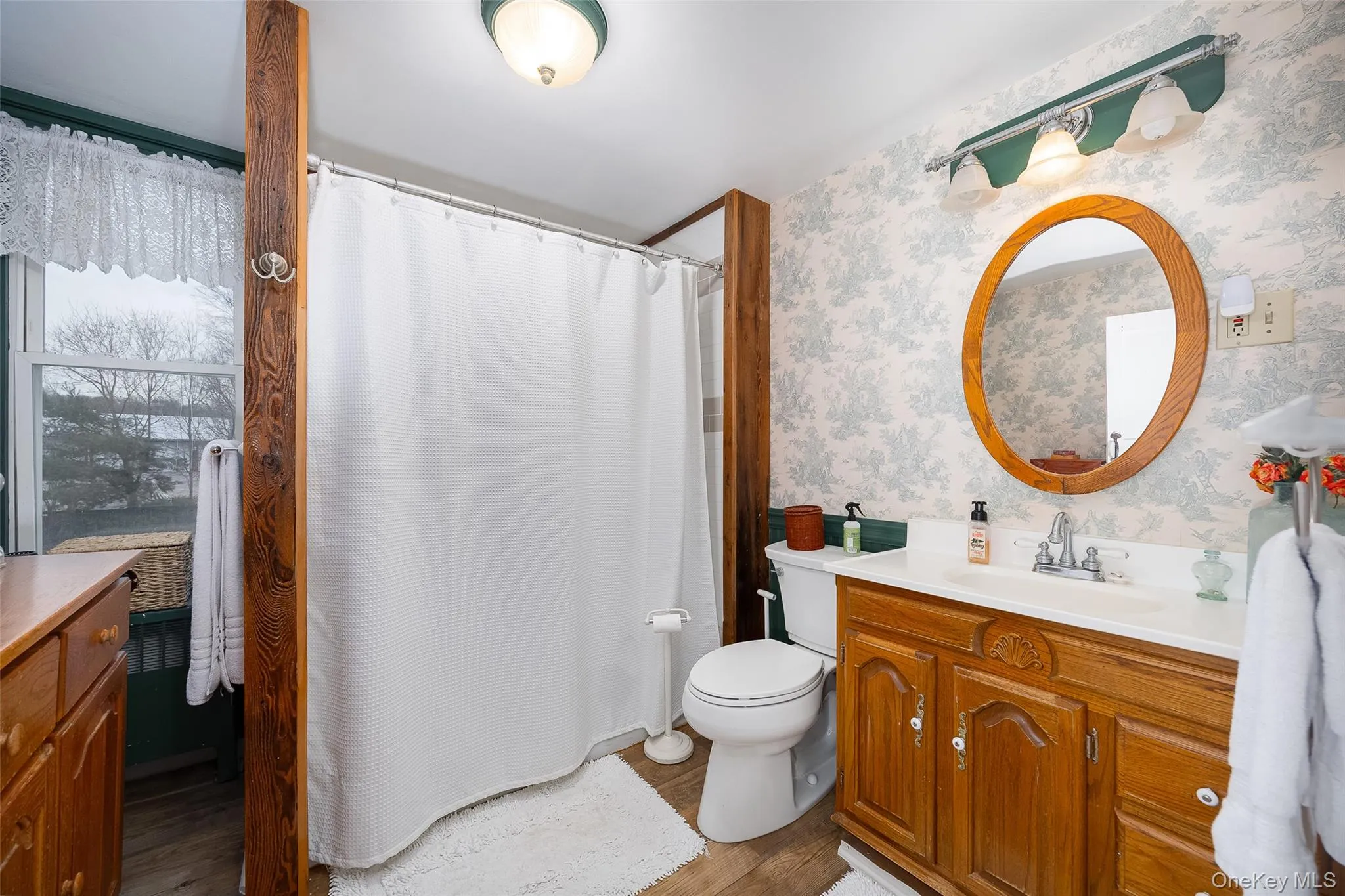 Bathroom with wallpapered walls, vanity, a shower with shower curtain, and dark wood-style floors Bathroom with wallpapered walls, vanity, a shower with shower curtain, and dark wood-style floors