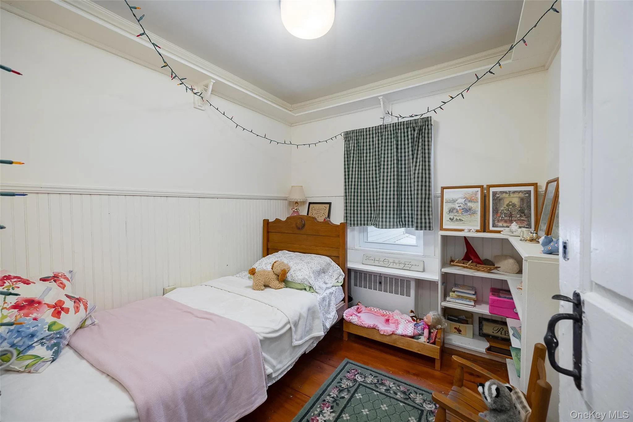 Bedroom with wood finished floors, radiator, ornamental molding, and wainscoting Bedroom with wood finished floors, radiator, ornamental molding, and wainscoting