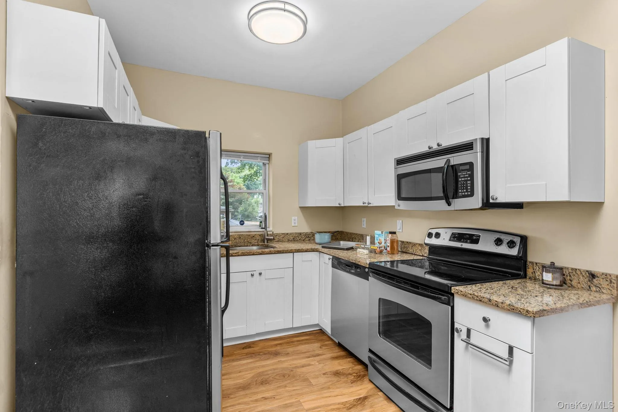 Well-appointed kitchen featuring white cabinetry, granite-finish countertops, stainless steel appliances, a built-in microwave, and wood-finish flooring. Well-appointed kitchen featuring white cabinetry, granite-finish countertops, stainless steel appliances, a built-in microwave, and wood-finish flooring.