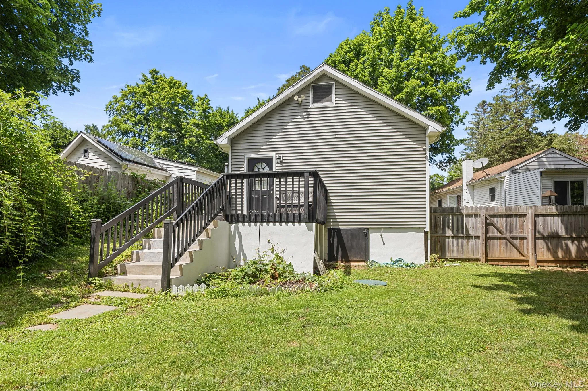 Rear exterior featuring horizontal siding, a private wood deck with dark railings, and a concrete staircase leading to a ground-level patio. Rear exterior featuring horizontal siding, a private wood deck with dark railings, and a concrete staircase leading to a ground-level patio.