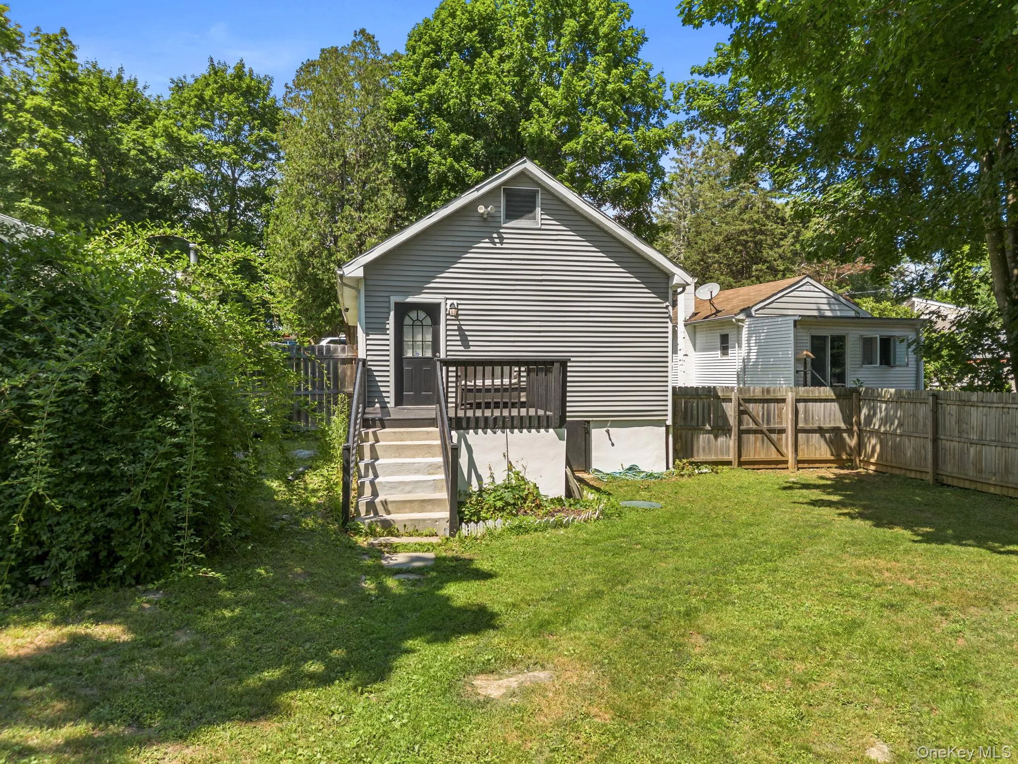 Rear exterior featuring gray horizontal siding, a dark wood deck, and concrete steps leading to a dark entry door Rear exterior featuring gray horizontal siding, a dark wood deck, and concrete steps leading to a dark entry door