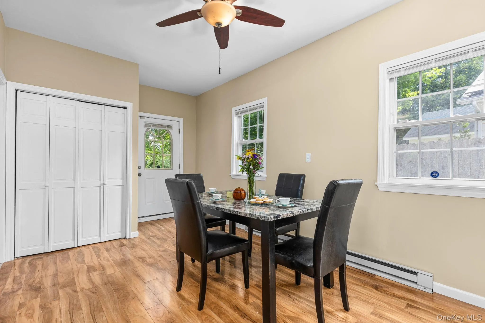 Dining area featuring wood-finish flooring, light beige wall paint, a white paneled bi-fold door, and multiple windows Dining area featuring wood-finish flooring, light beige wall paint, a white paneled bi-fold door, and multiple windows