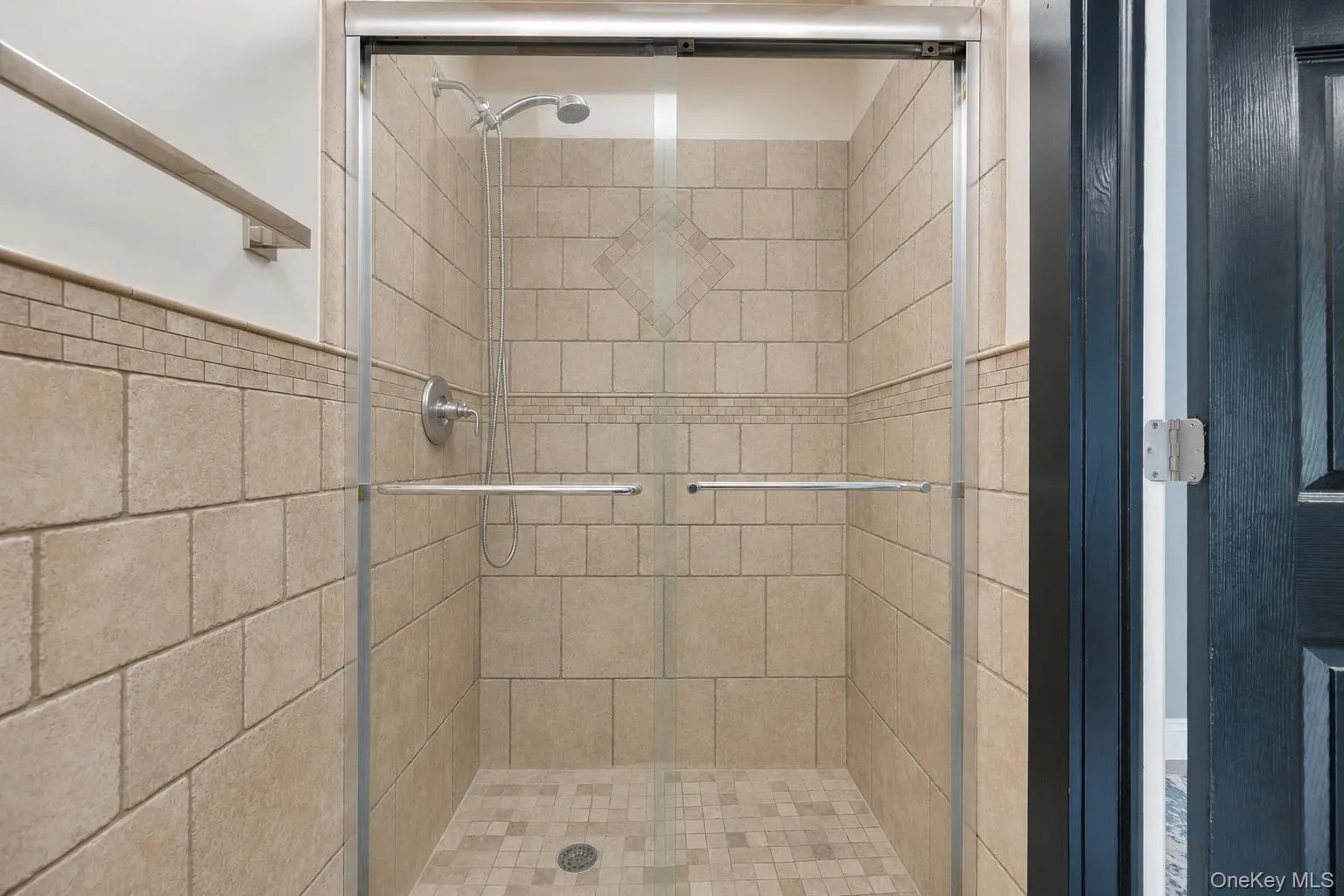 Tiled shower stall featuring clear glass enclosure with brushed nickel hardware, a decorative wall tile band, and a matching tiled shower pan Tiled shower stall featuring clear glass enclosure with brushed nickel hardware, a decorative wall tile band, and a matching tiled shower pan