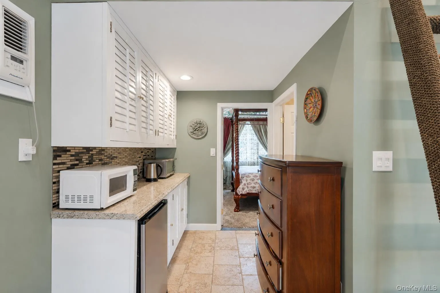 Galley area featuring white shaker-style cabinetry with louvered doors, a mosaic tile backsplash, and a granite-finish countertop Galley area featuring white shaker-style cabinetry with louvered doors, a mosaic tile backsplash, and a granite-finish countertop