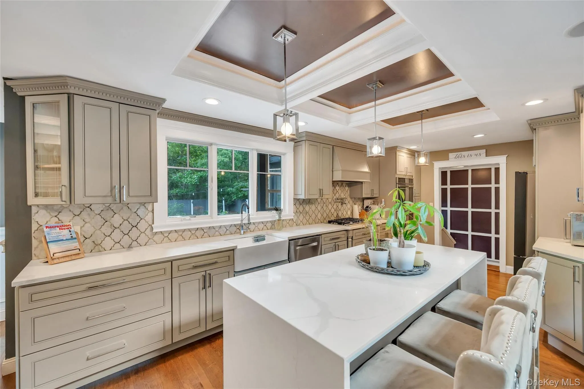 Expansive kitchen featuring a large central island with seating, a deep farmhouse-style sink, a patterned tile backsplash, and recessed and pendant lighting fixtures Expansive kitchen featuring a large central island with seating, a deep farmhouse-style sink, a patterned tile backsplash, and recessed and pendant lighting fixtures