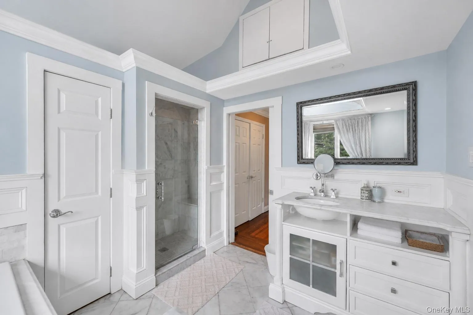 Bathroom featuring a glass-enclosed shower, white vanity with an undermount sink, marble-finish countertop, and decorative mirror Bathroom featuring a glass-enclosed shower, white vanity with an undermount sink, marble-finish countertop, and decorative mirror