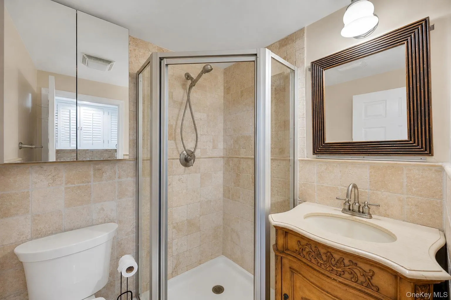 Bathroom featuring a corner shower with a glass enclosure, a vanity with an ornate wood-finish base and light-colored countertop, and a decorative framed mirror Bathroom featuring a corner shower with a glass enclosure, a vanity with an ornate wood-finish base and light-colored countertop, and a decorative framed mirror