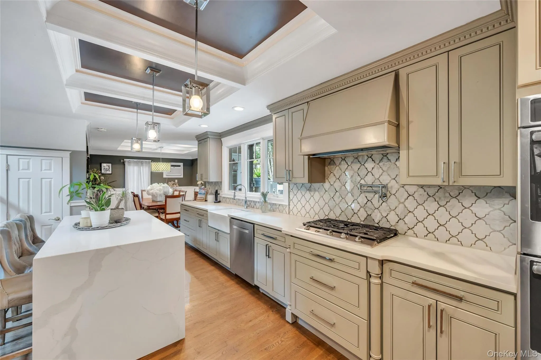 Kitchen featuring a waterfall island with a light-toned countertop, pendant lighting, recessed lighting, wood-finish flooring, and light-toned cabinetry with a decorative backsplash Kitchen featuring a waterfall island with a light-toned countertop, pendant lighting, recessed lighting, wood-finish flooring, and light-toned cabinetry with a decorative backsplash