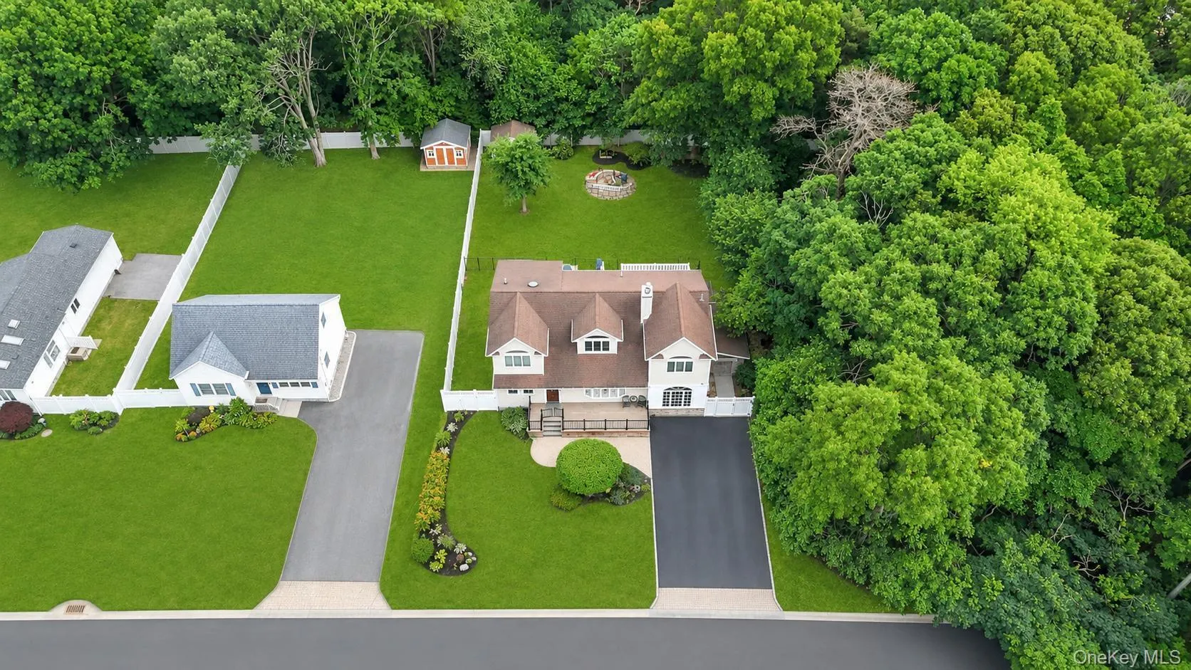 Expansive property featuring a multi-level residence with a brown shingle roof and white siding, an attached paved driveway, and a manicured lawn Expansive property featuring a multi-level residence with a brown shingle roof and white siding, an attached paved driveway, and a manicured lawn