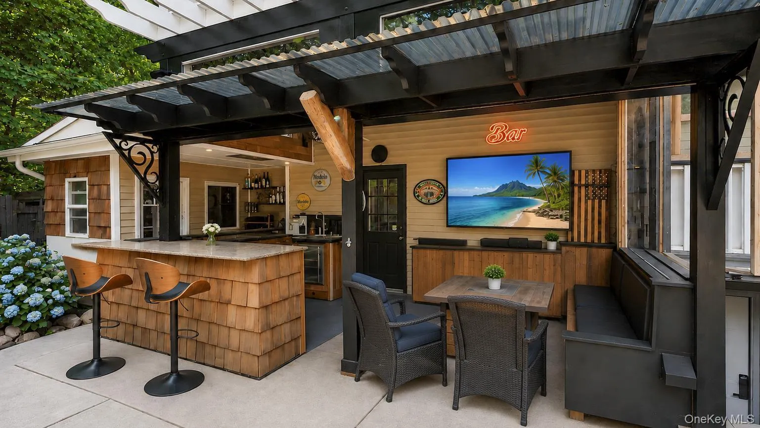 Outdoor entertainment area featuring a corrugated metal roof, wood shake bar with a stone countertop, built-in media console with television, exterior wall-mounted lighting, and integrated bench seating Outdoor entertainment area featuring a corrugated metal roof, wood shake bar with a stone countertop, built-in media console with television, exterior wall-mounted lighting, and integrated bench seating