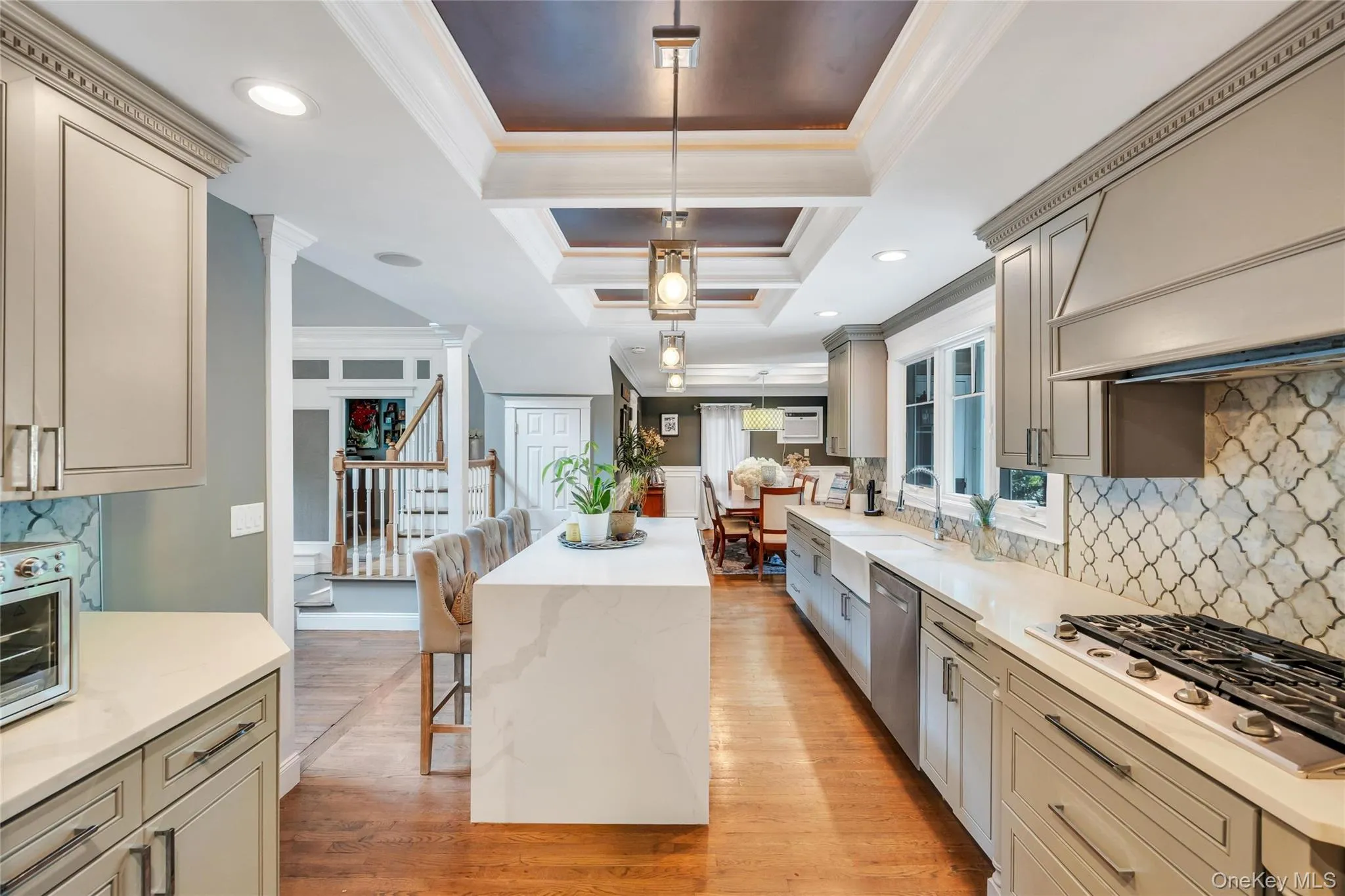 Gourmet kitchen with a waterfall edge island, recessed lighting, coffered ceiling detail, gas range, and geometric tile backsplash Gourmet kitchen with a waterfall edge island, recessed lighting, coffered ceiling detail, gas range, and geometric tile backsplash