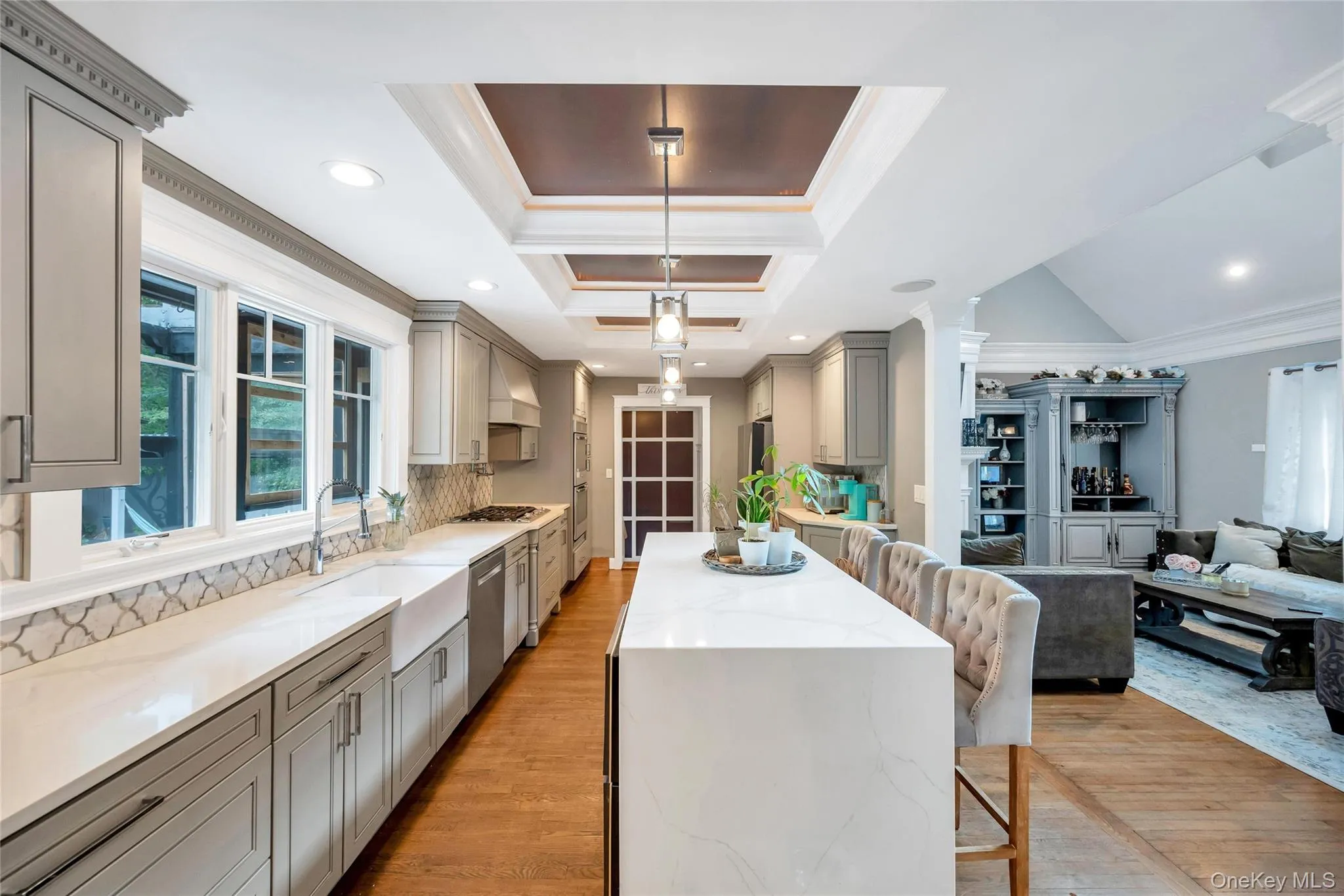 Spacious kitchen featuring an expansive island with seating, a farmhouse sink, stainless steel appliances, and gray cabinetry Spacious kitchen featuring an expansive island with seating, a farmhouse sink, stainless steel appliances, and gray cabinetry
