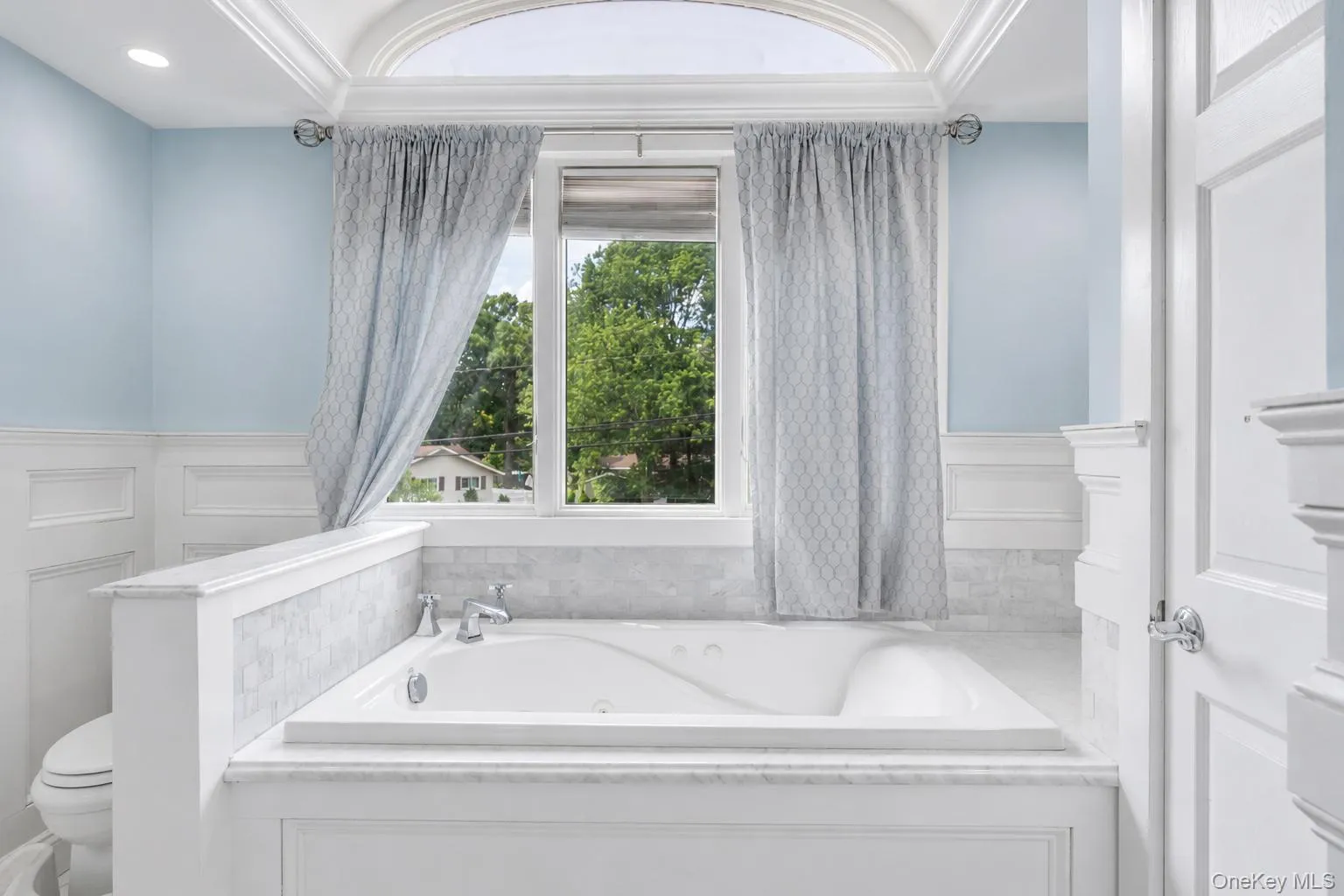 Deep soaking tub with polished chrome fixtures, surrounded by white wainscoting and light marble-finish tile Deep soaking tub with polished chrome fixtures, surrounded by white wainscoting and light marble-finish tile