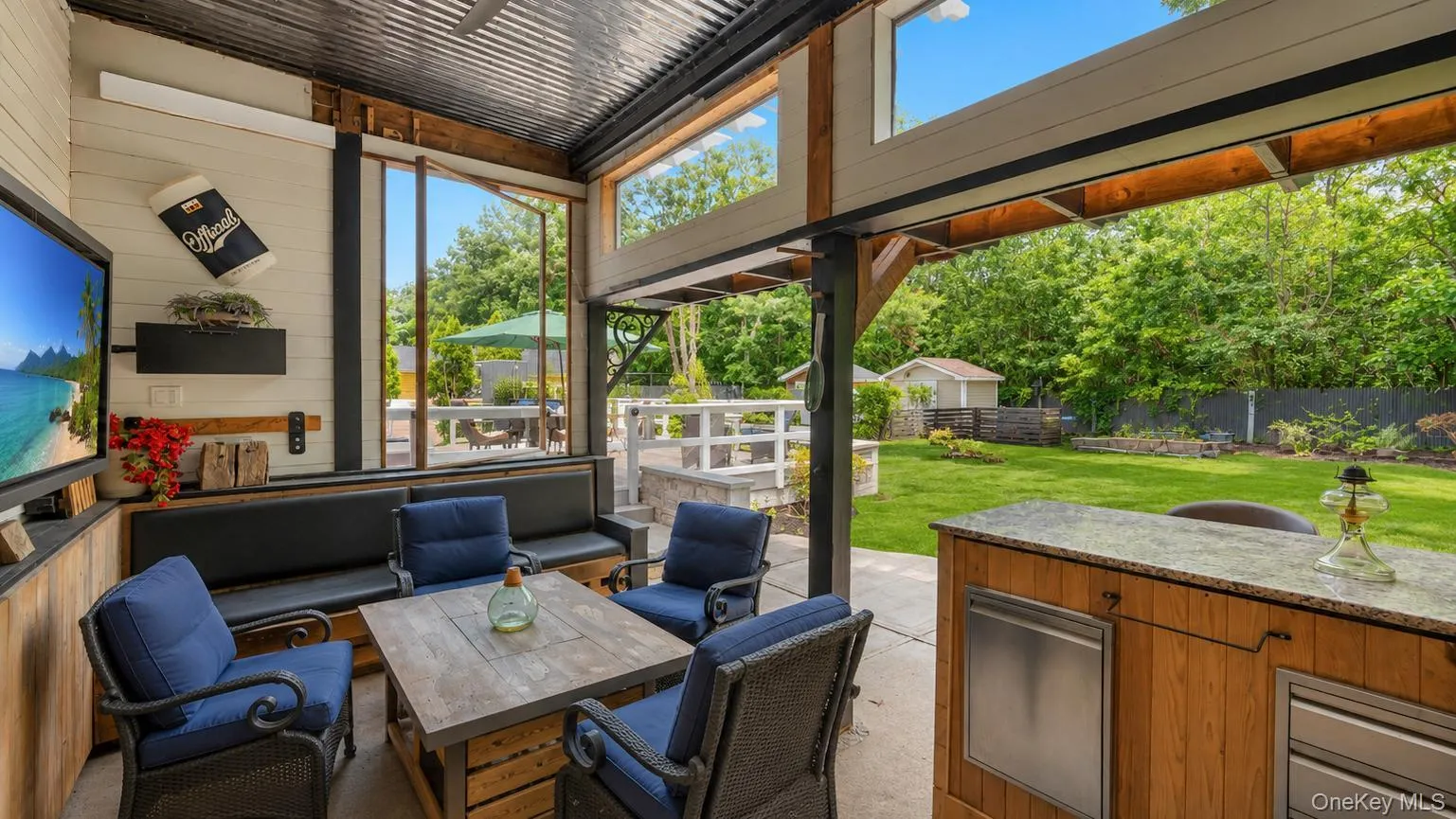 Outdoor entertainment area featuring a corrugated metal roof, wood shake bar with a stone countertop, built-in media console with television, exterior wall-mounted lighting, and integrated bench seating Outdoor entertainment area featuring a corrugated metal roof, wood shake bar with a stone countertop, built-in media console with television, exterior wall-mounted lighting, and integrated bench seating