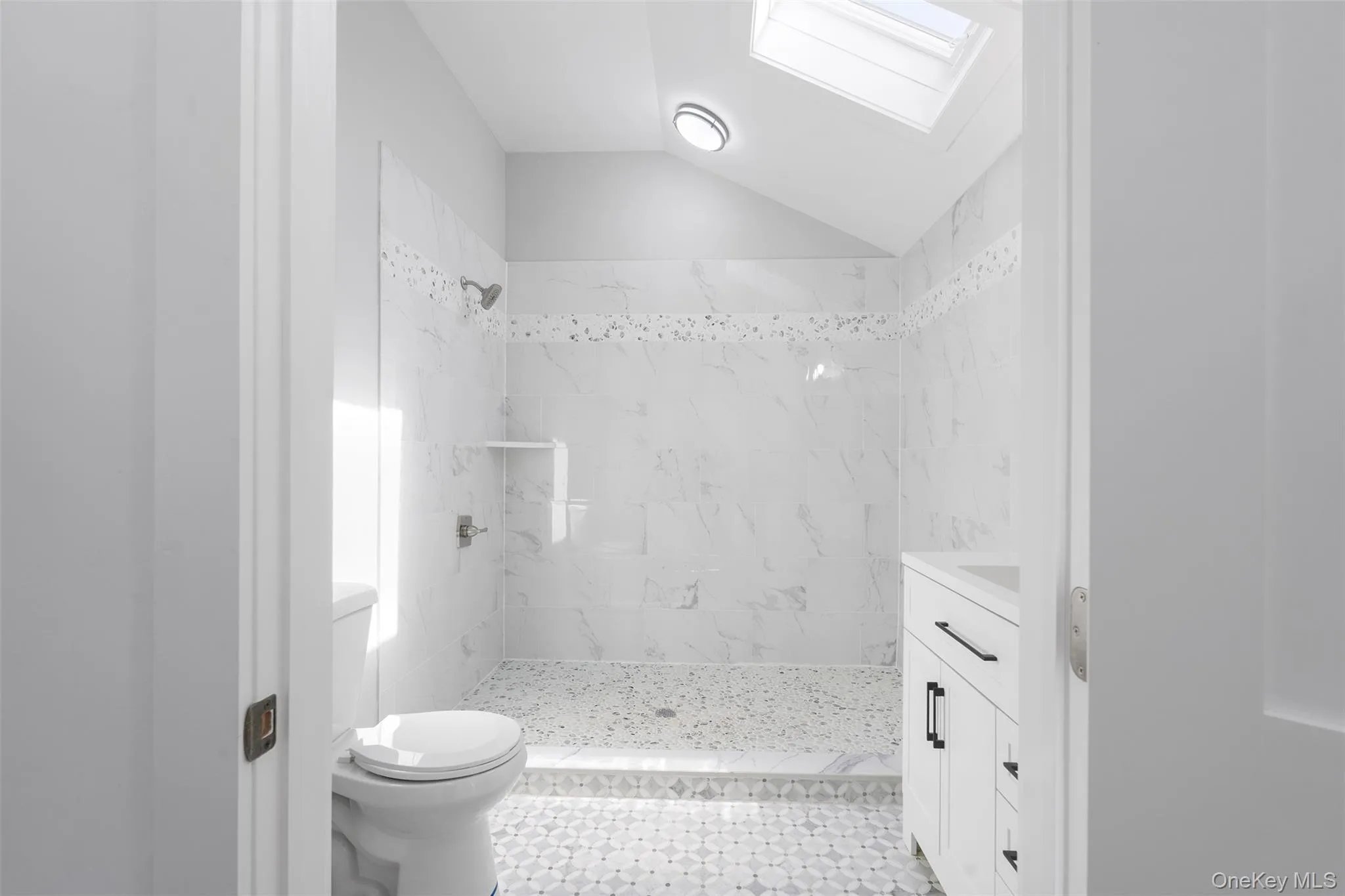 Bathroom featuring a stall shower, a skylight, vanity, vaulted ceiling, and tile patterned flooring Bathroom featuring a stall shower, a skylight, vanity, vaulted ceiling, and tile patterned flooring