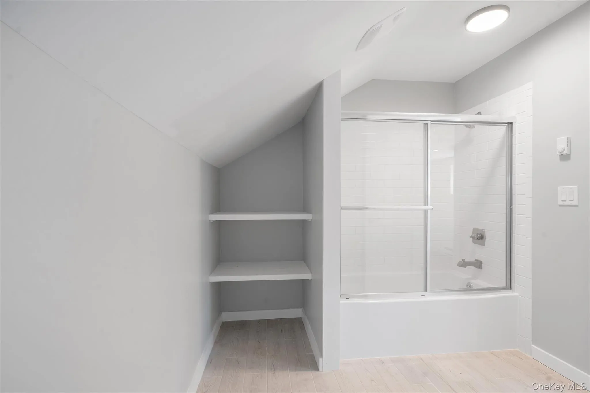 Bathroom featuring lofted ceiling, shower / bath combination with glass door, and wood finished floors Bathroom featuring lofted ceiling, shower / bath combination with glass door, and wood finished floors