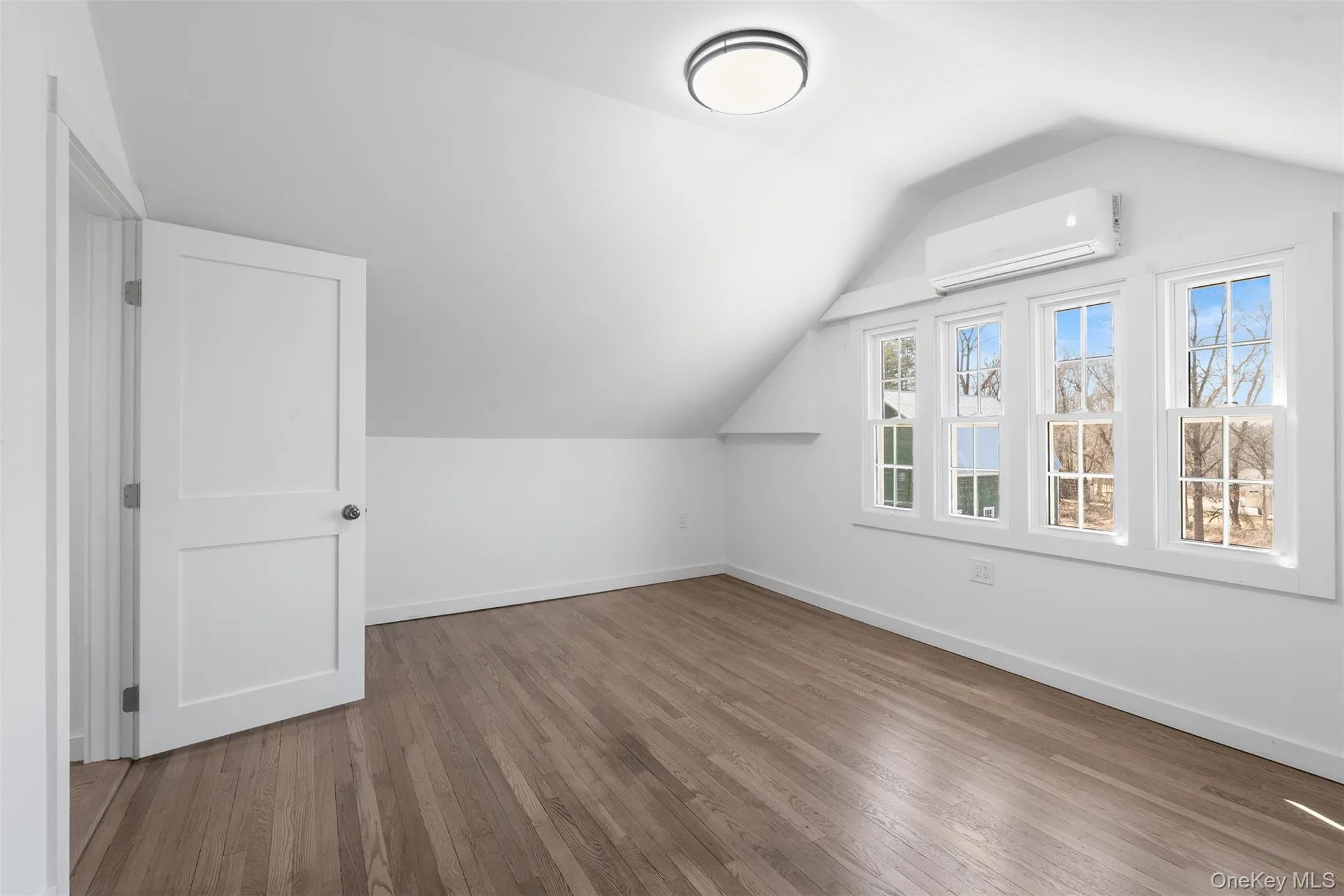 Additional living space featuring a wall mounted air conditioner, lofted ceiling, and wood finished floors Additional living space featuring a wall mounted air conditioner, lofted ceiling, and wood finished floors
