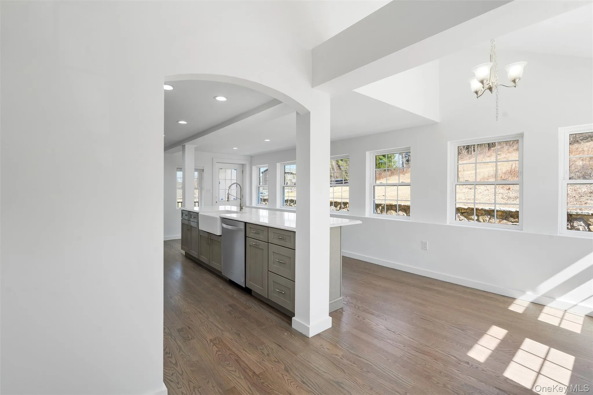 Kitchen featuring gray cabinetry, arched walkways, dark wood-style flooring, stainless steel dishwasher, and light countertops Kitchen featuring gray cabinetry, arched walkways, dark wood-style flooring, stainless steel dishwasher, and light countertops