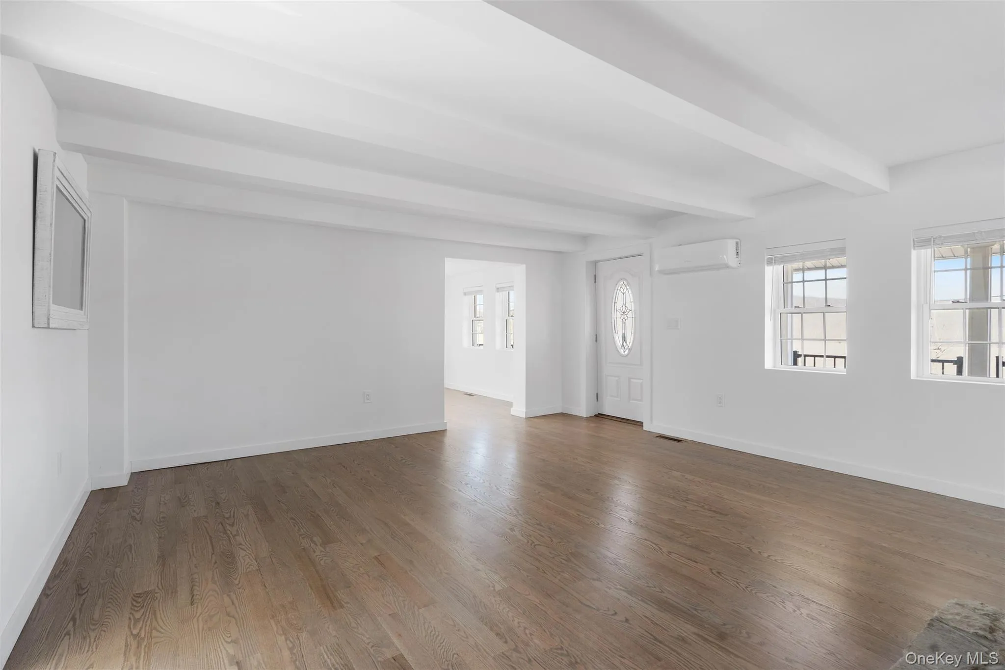 Unfurnished living room with a wall mounted AC, beamed ceiling, and dark wood finished floors Unfurnished living room with a wall mounted AC, beamed ceiling, and dark wood finished floors
