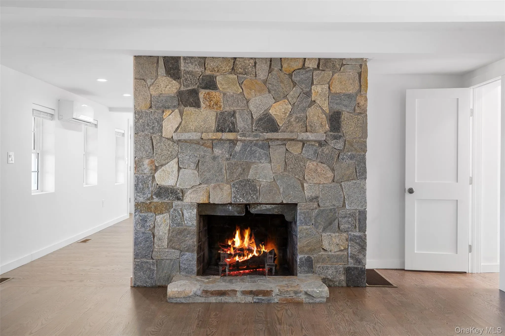 Detailed view of a fireplace, wood finished floors, and a wall mounted AC Detailed view of a fireplace, wood finished floors, and a wall mounted AC