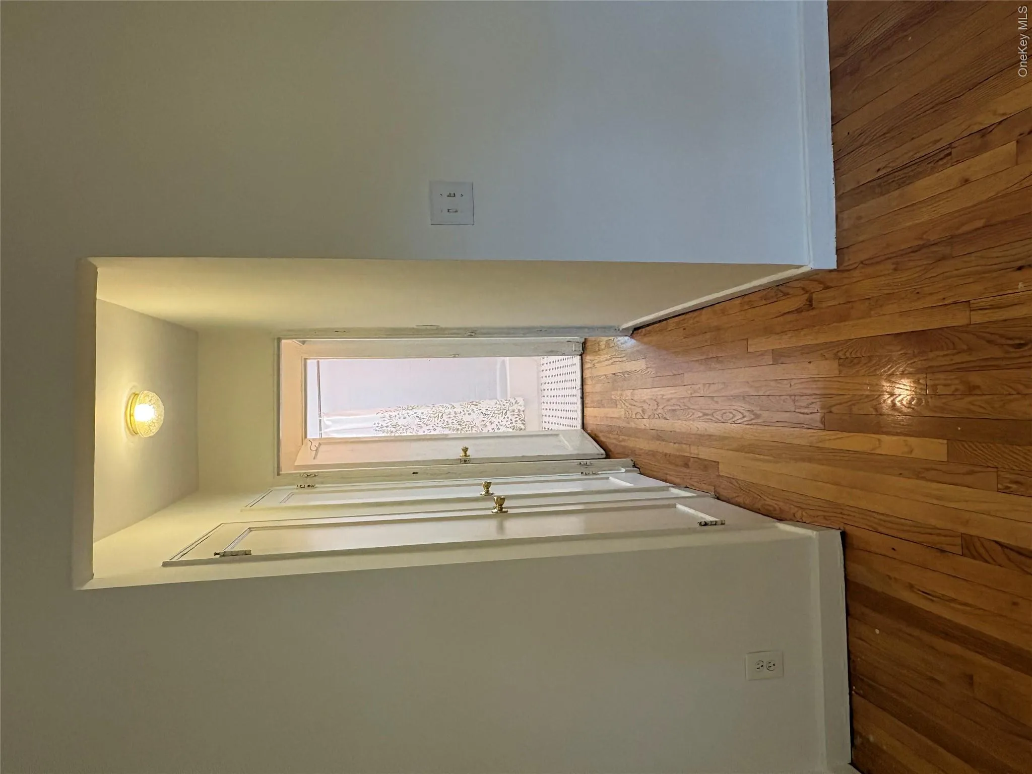 Hardwood flooring extending through a hallway with white paneled doors and a ceiling-mounted light fixture. View from Bedroom- down hallway to bathroom. Hardwood flooring extending through a hallway with white paneled doors and a ceiling-mounted light fixture. View from Bedroom- down hallway to bathroom.