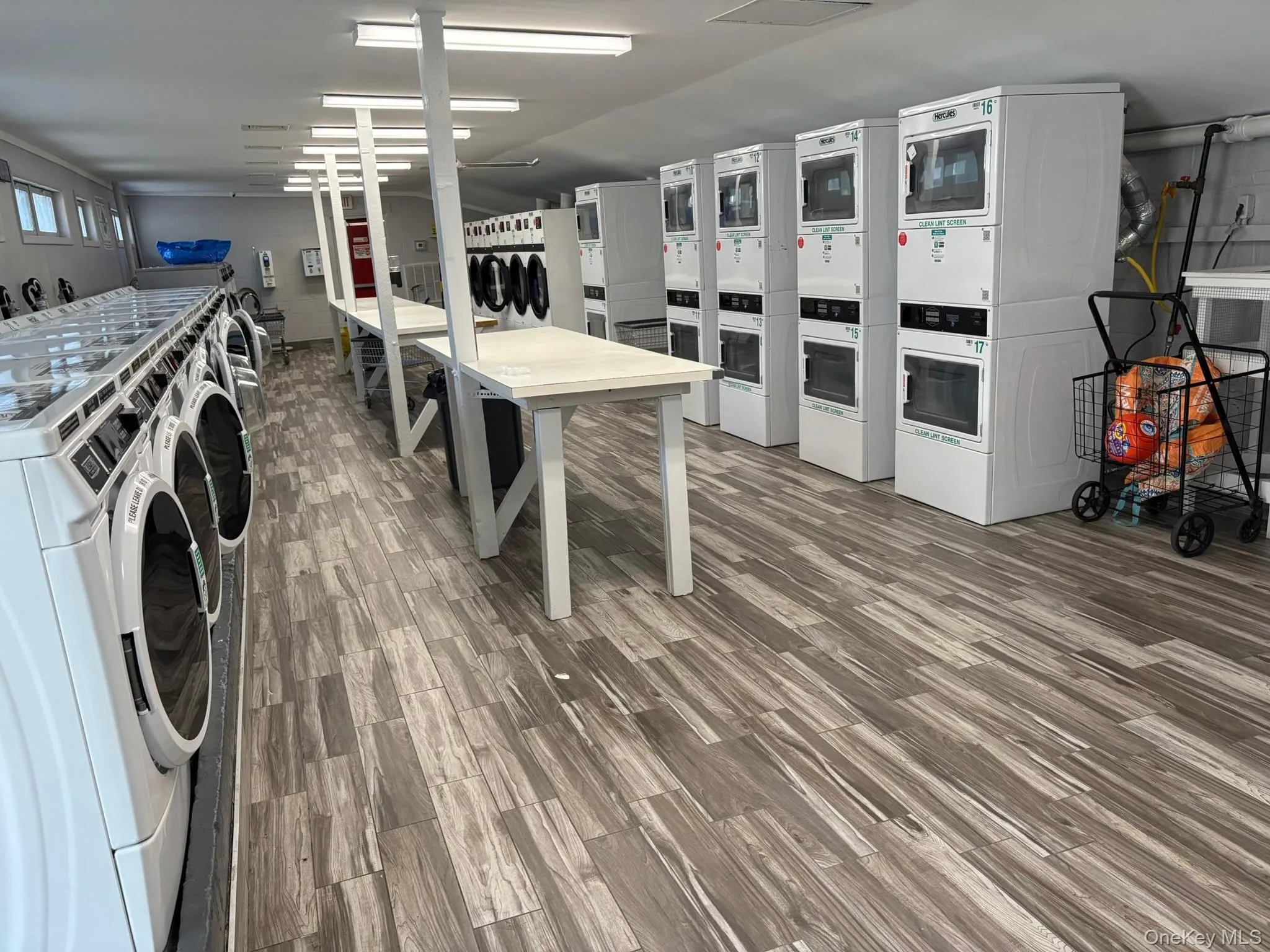 Commercial laundry facility featuring wood-finish flooring, white walls, and fluorescent ceiling lights Commercial laundry facility featuring wood-finish flooring, white walls, and fluorescent ceiling lights