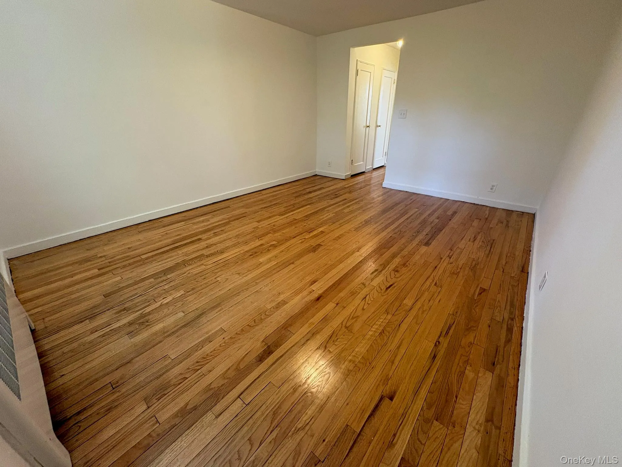Hardwood flooring throughout a room with white painted walls and white baseboards. View from window side. Hardwood flooring throughout a room with white painted walls and white baseboards. View from window side.