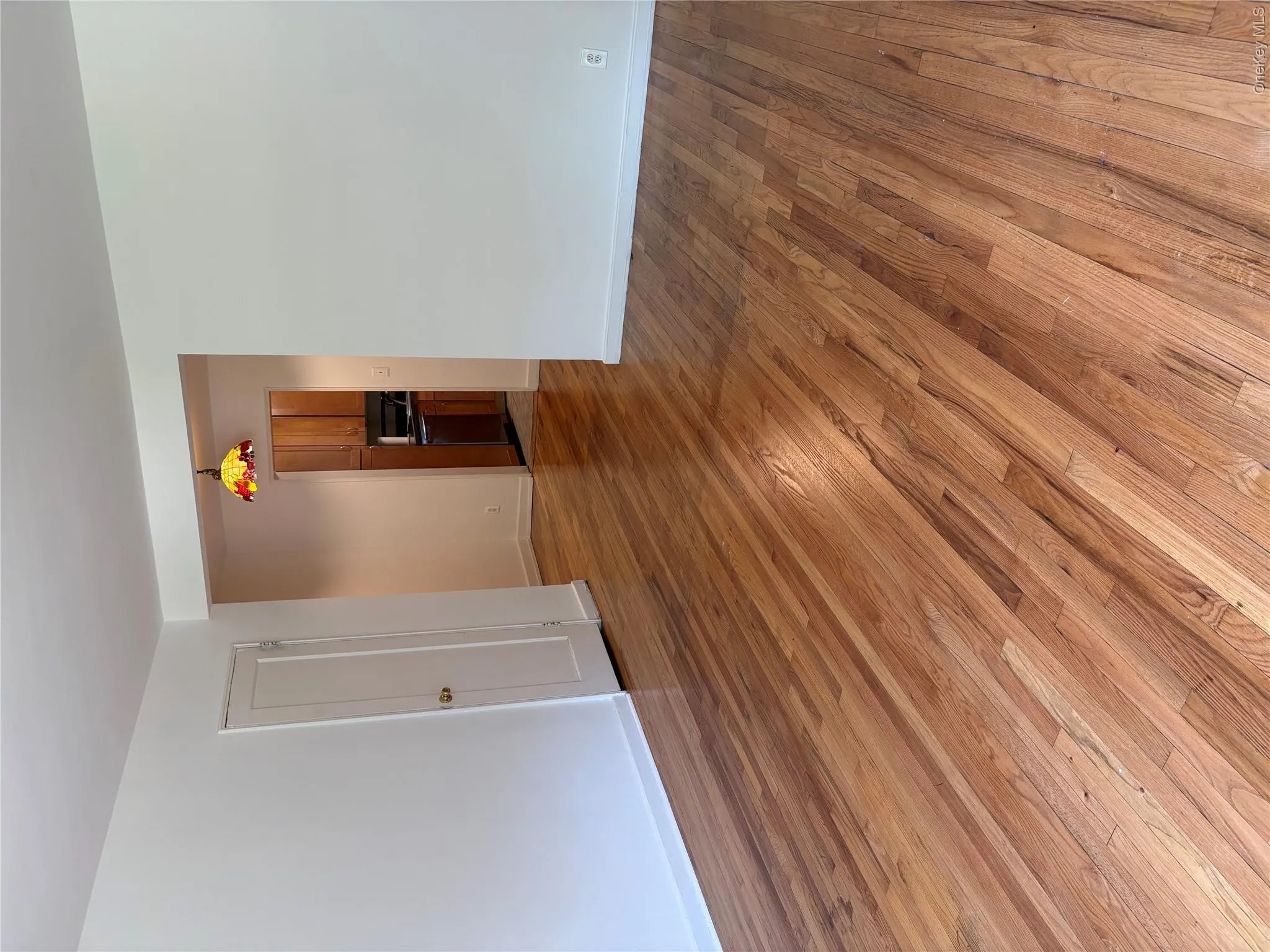 Hardwood flooring throughout a room with white painted walls and white baseboards. Front entrance view. Hardwood flooring throughout a room with white painted walls and white baseboards. Front entrance view.