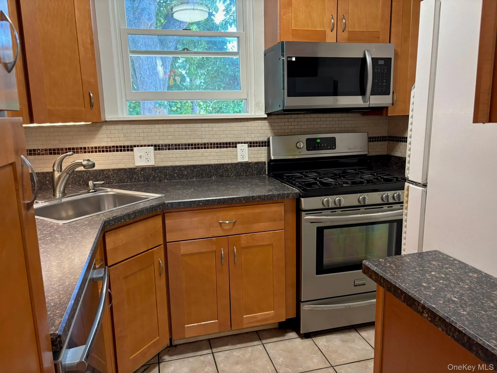 The kitchen features light wood-finish cabinetry, dark speckled countertops, and a mosaic tile backsplash The kitchen features light wood-finish cabinetry, dark speckled countertops, and a mosaic tile backsplash