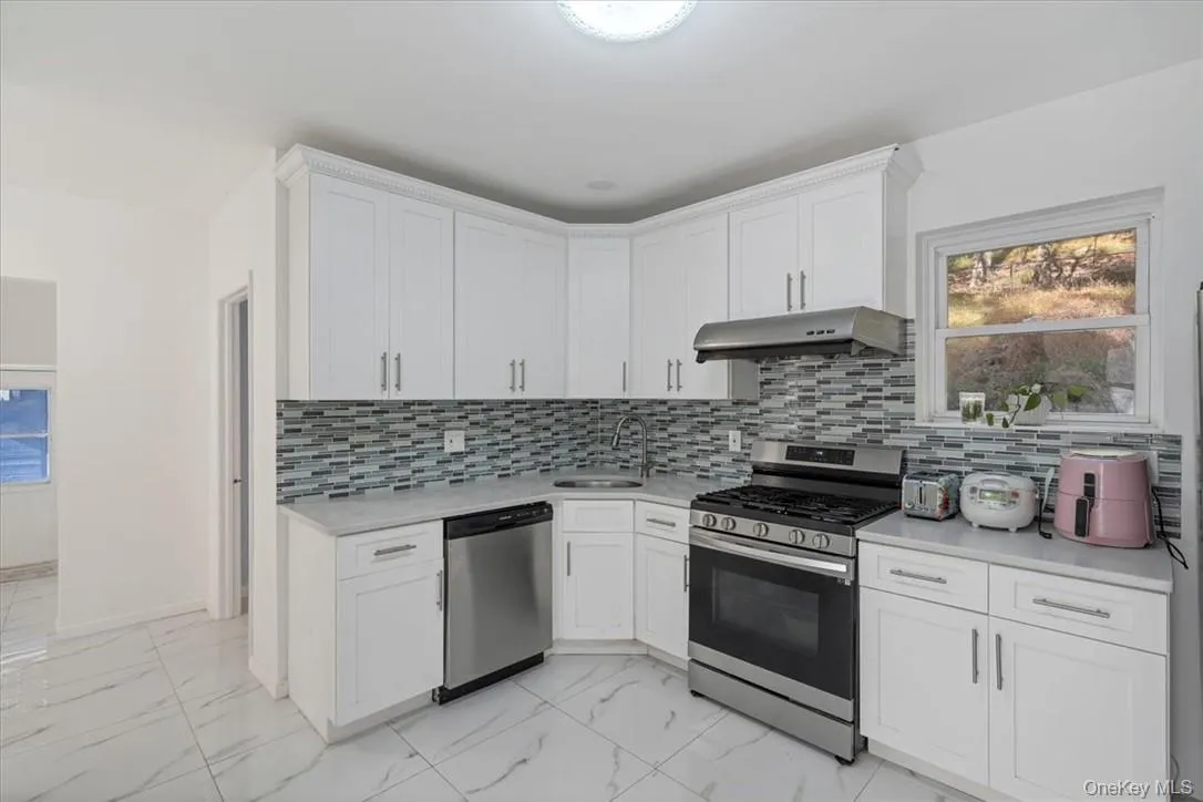 Kitchen featuring decorative backsplash, sink, stainless steel appliances, and white cabinets Kitchen featuring decorative backsplash, sink, stainless steel appliances, and white cabinets