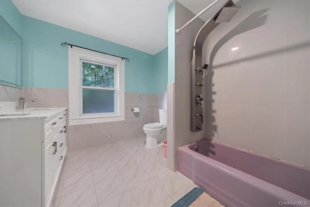Full bathroom featuring vanity, tile walls, toilet, and tiled shower / bath combo Full bathroom featuring vanity, tile walls, toilet, and tiled shower / bath combo