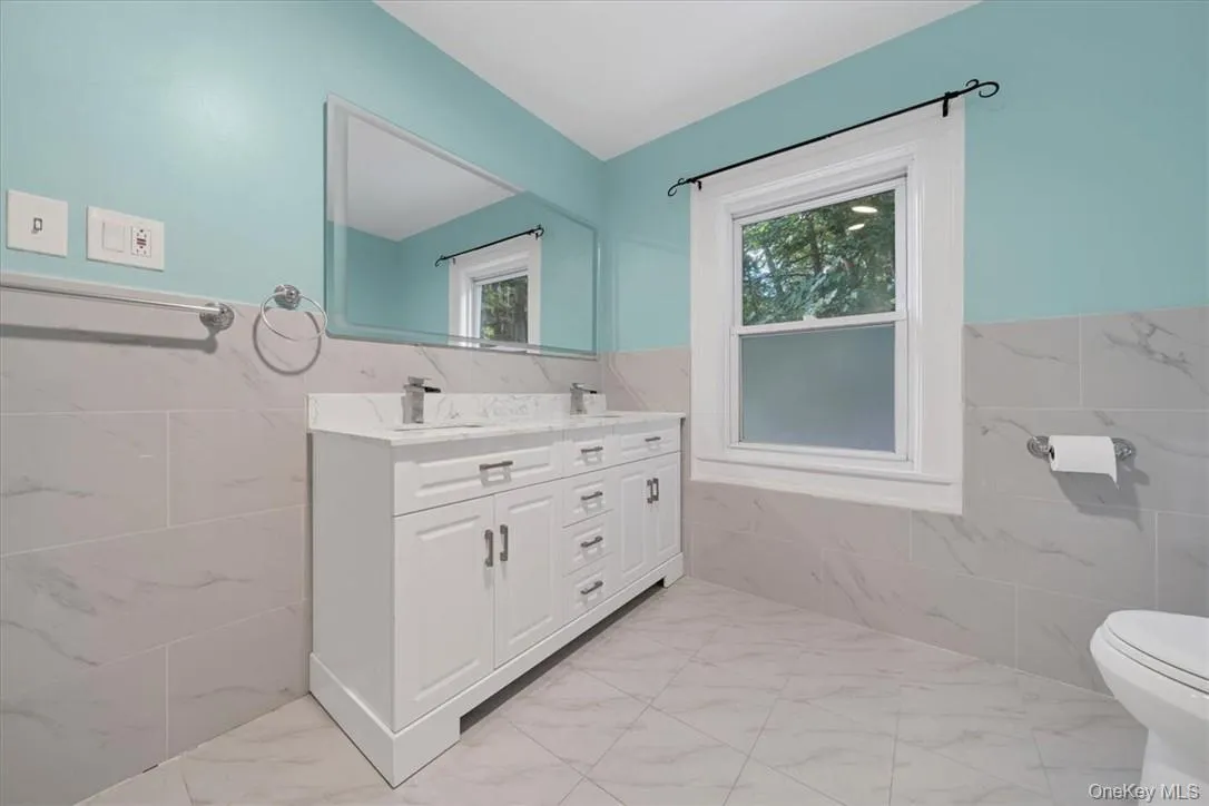 Bathroom featuring a healthy amount of sunlight, vanity, tile walls, and toilet Bathroom featuring a healthy amount of sunlight, vanity, tile walls, and toilet