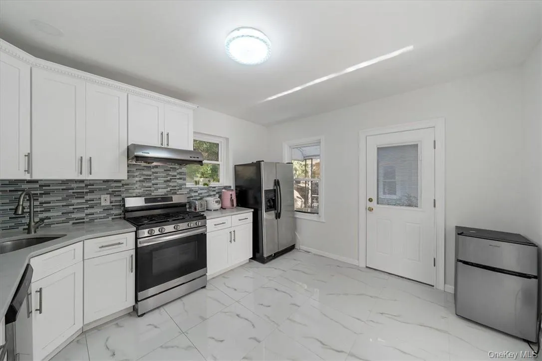Kitchen with appliances with stainless steel finishes, sink, tasteful backsplash, and white cabinetry Kitchen with appliances with stainless steel finishes, sink, tasteful backsplash, and white cabinetry