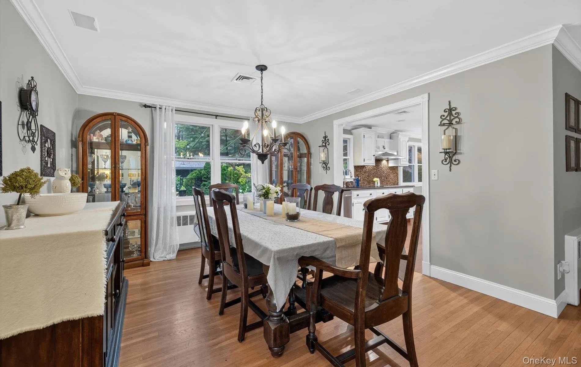 Dining area featuring wood-finish flooring, light grey painted walls, white crown molding, and a chandelier with candelabra lights Dining area featuring wood-finish flooring, light grey painted walls, white crown molding, and a chandelier with candelabra lights
