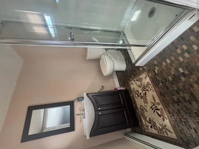 Three-quarter bathroom featuring a stall shower with a clear glass enclosure, a dark wood-finish vanity with a white basin sink, and a framed mirror Three-quarter bathroom featuring a stall shower with a clear glass enclosure, a dark wood-finish vanity with a white basin sink, and a framed mirror