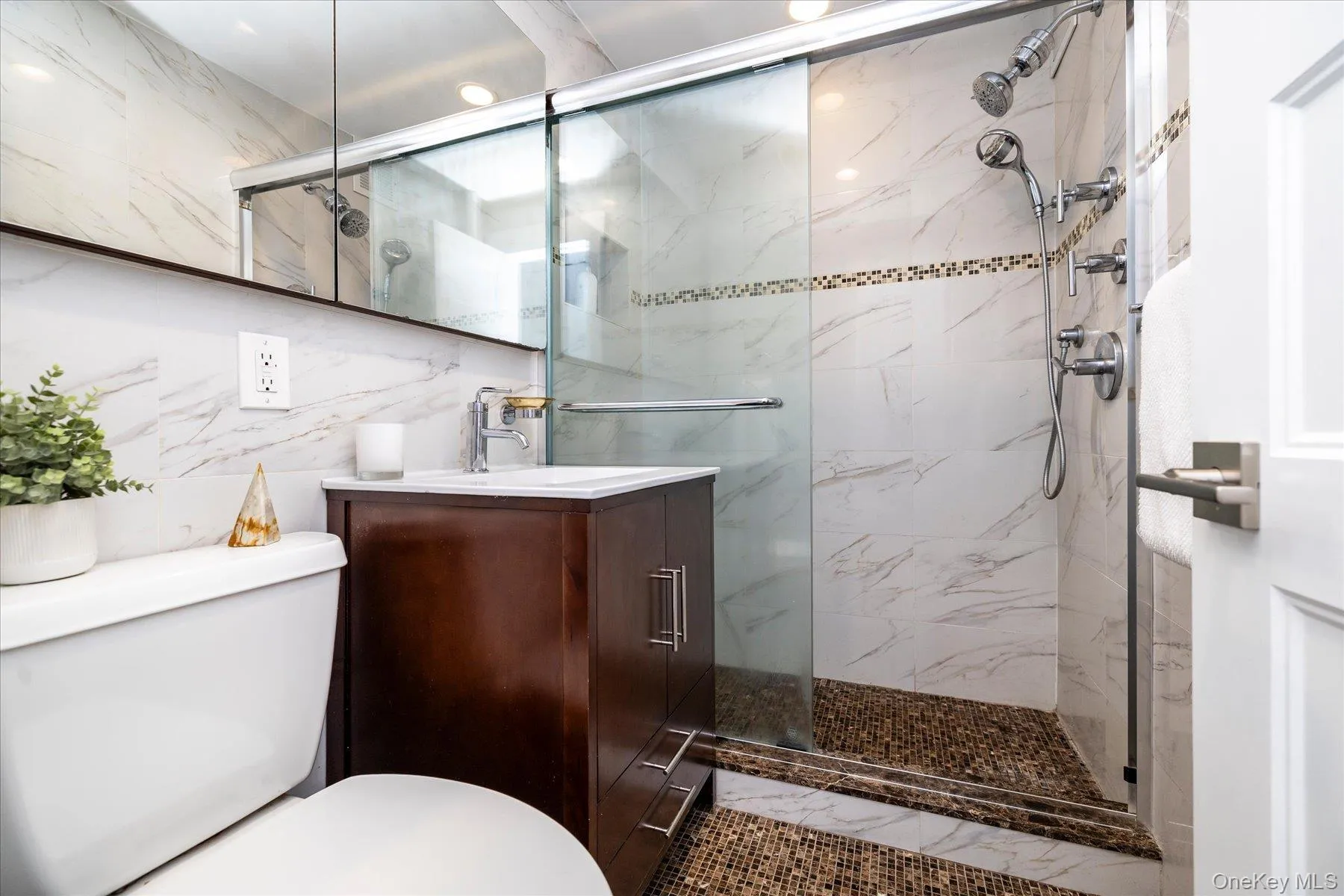 Bathroom featuring a walk-in shower with glass enclosure, white marble-look wall tiling, and pebble-style flooring Bathroom featuring a walk-in shower with glass enclosure, white marble-look wall tiling, and pebble-style flooring