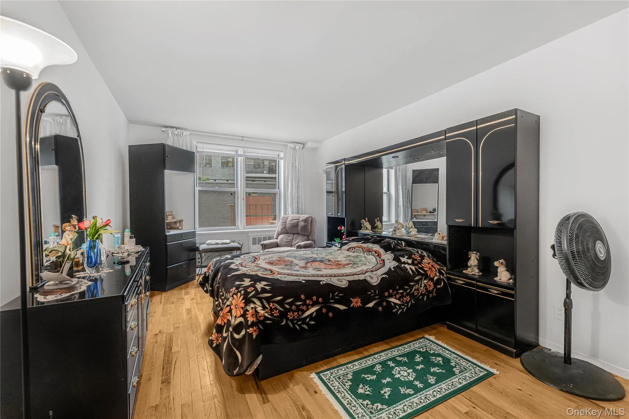 Spacious bedroom featuring wood-finish flooring, white walls, and a large window with natural light Spacious bedroom featuring wood-finish flooring, white walls, and a large window with natural light