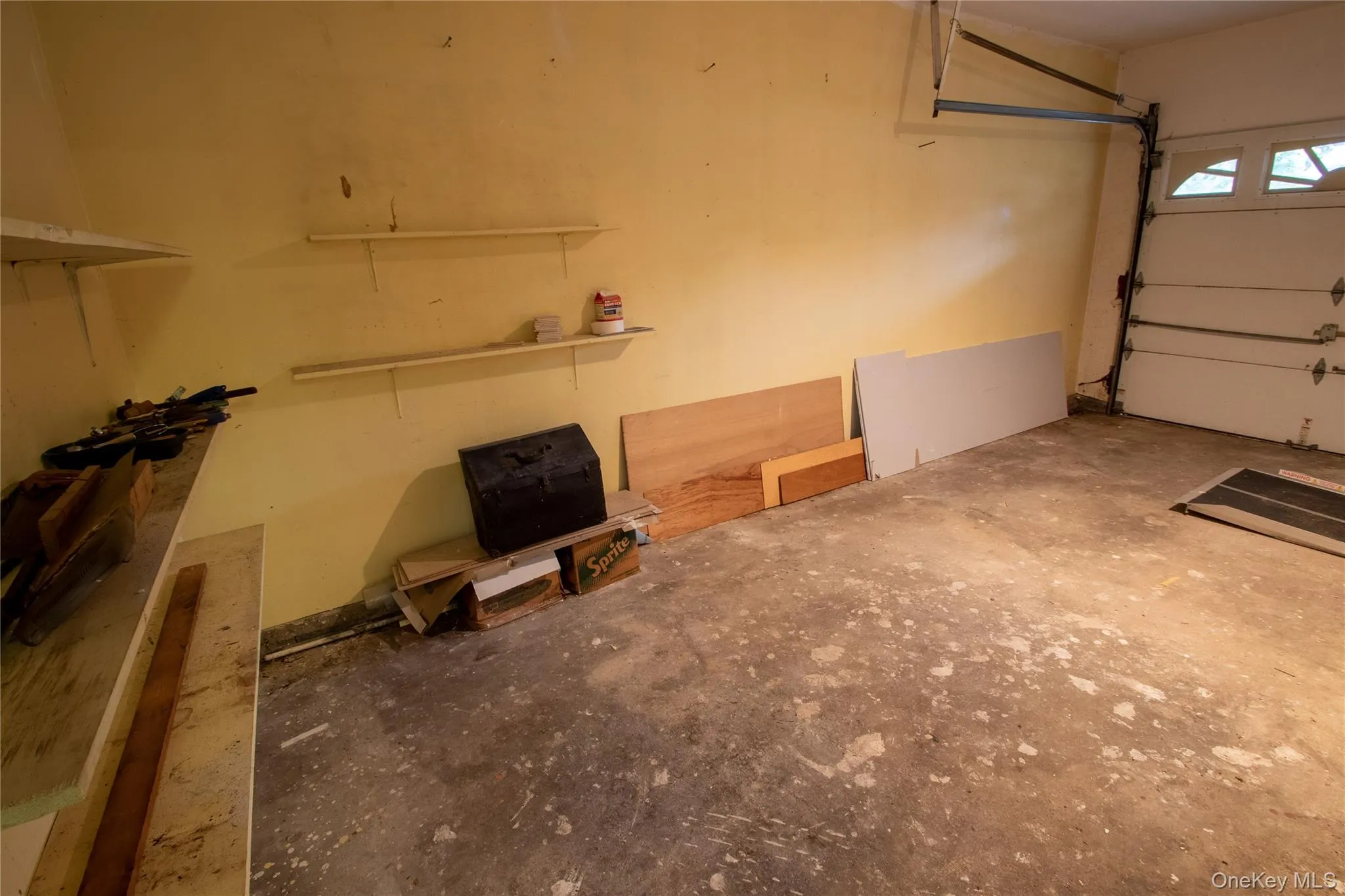 Spacious garage featuring a concrete floor, light yellow walls, and a white overhead garage door with upper window panels Spacious garage featuring a concrete floor, light yellow walls, and a white overhead garage door with upper window panels