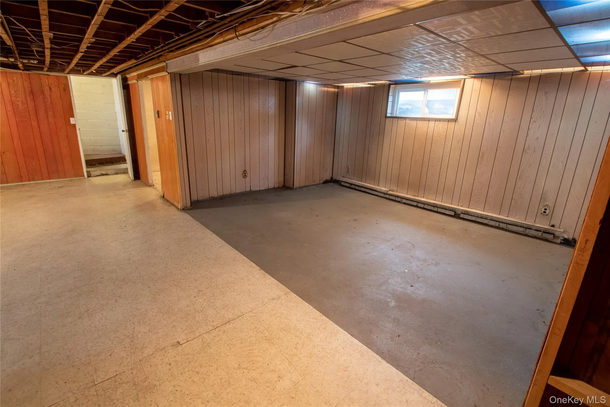 Finished basement area featuring wood-panel walls, a drop ceiling, and a visible window for natural light Finished basement area featuring wood-panel walls, a drop ceiling, and a visible window for natural light