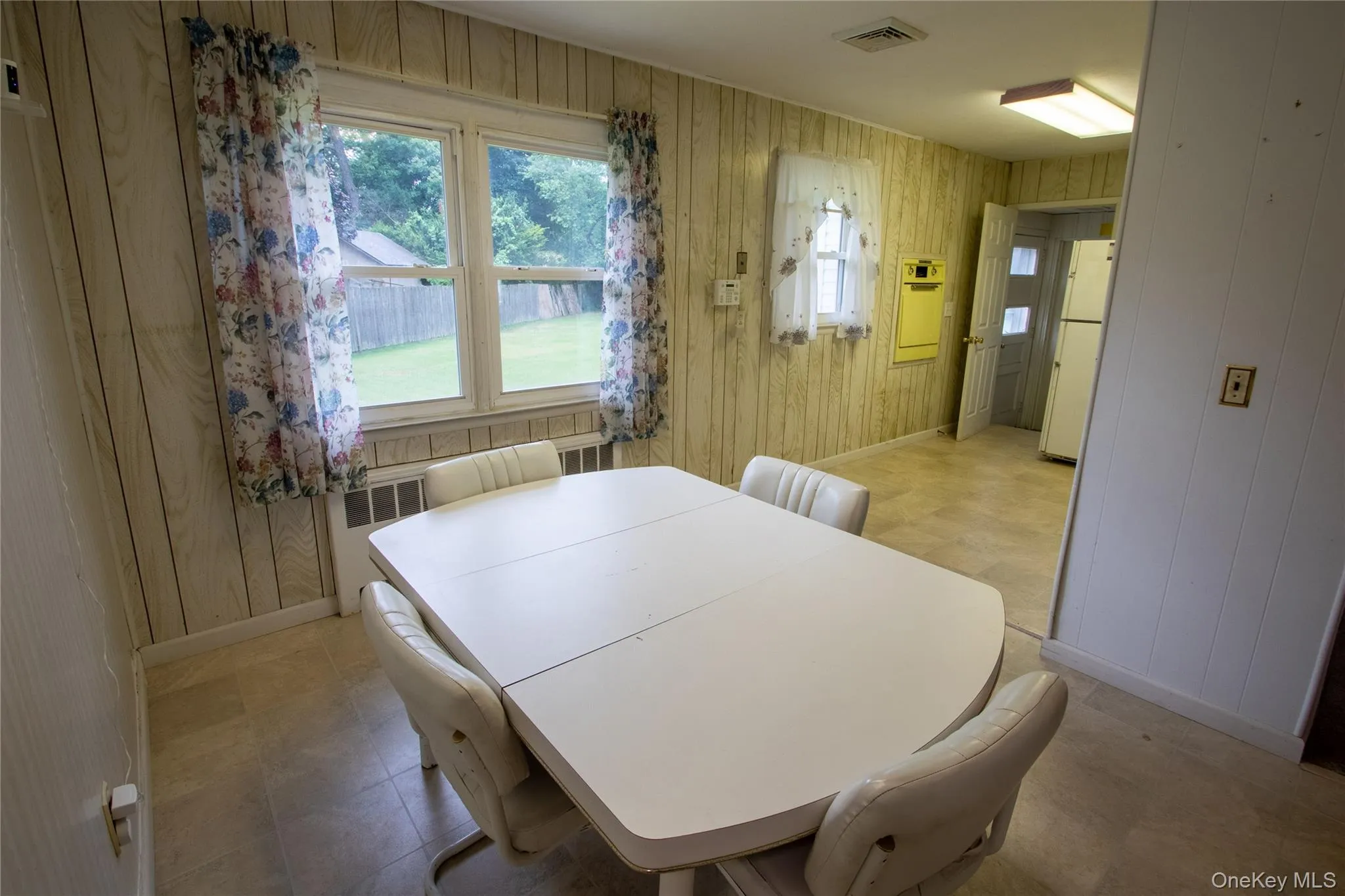 Dining area featuring wood-panel walls, light-toned flooring, a window offering exterior views, and a doorway opening to an adjacent room Dining area featuring wood-panel walls, light-toned flooring, a window offering exterior views, and a doorway opening to an adjacent room