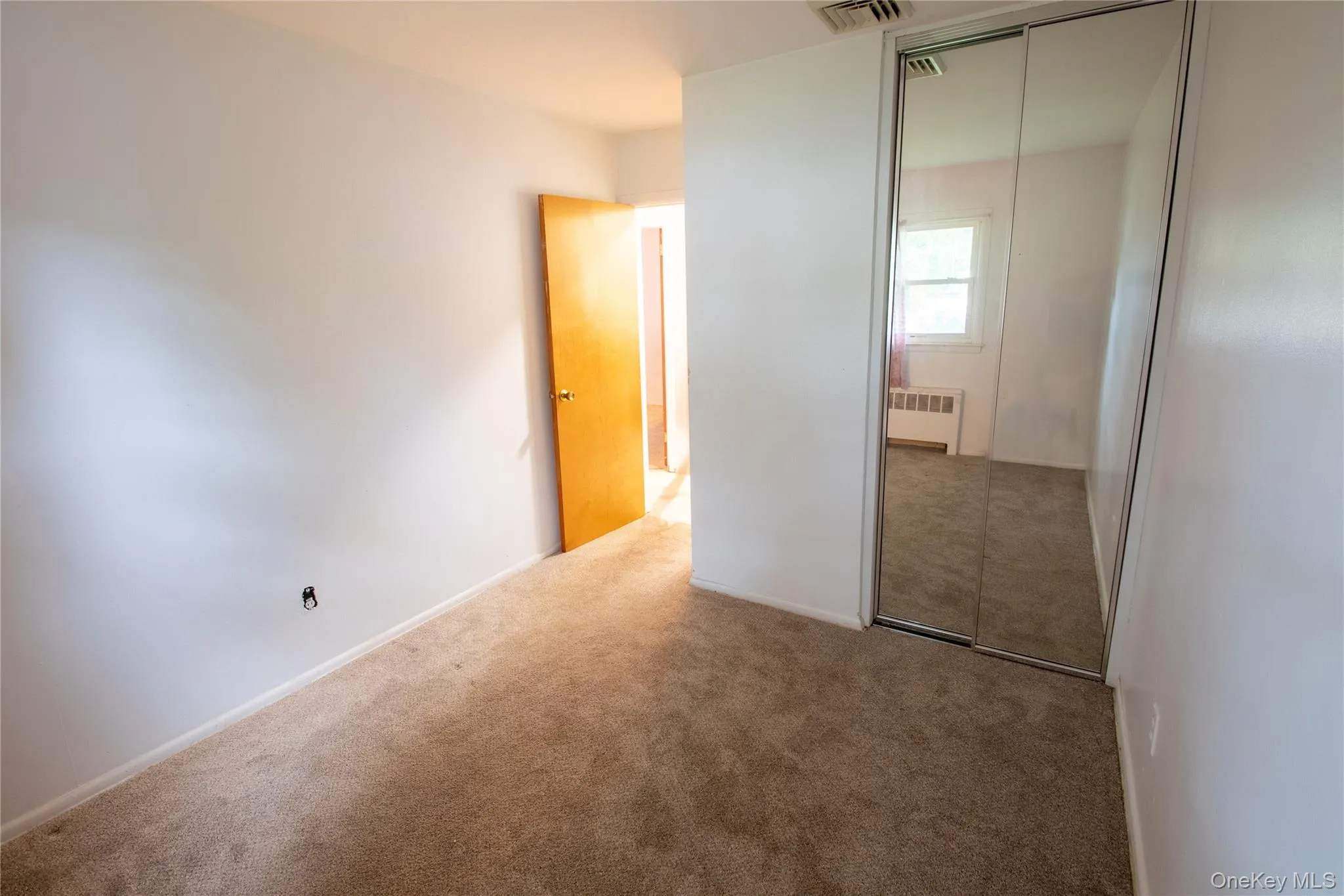Room featuring neutral-toned carpeting, white walls, and a light wood-finish door Room featuring neutral-toned carpeting, white walls, and a light wood-finish door