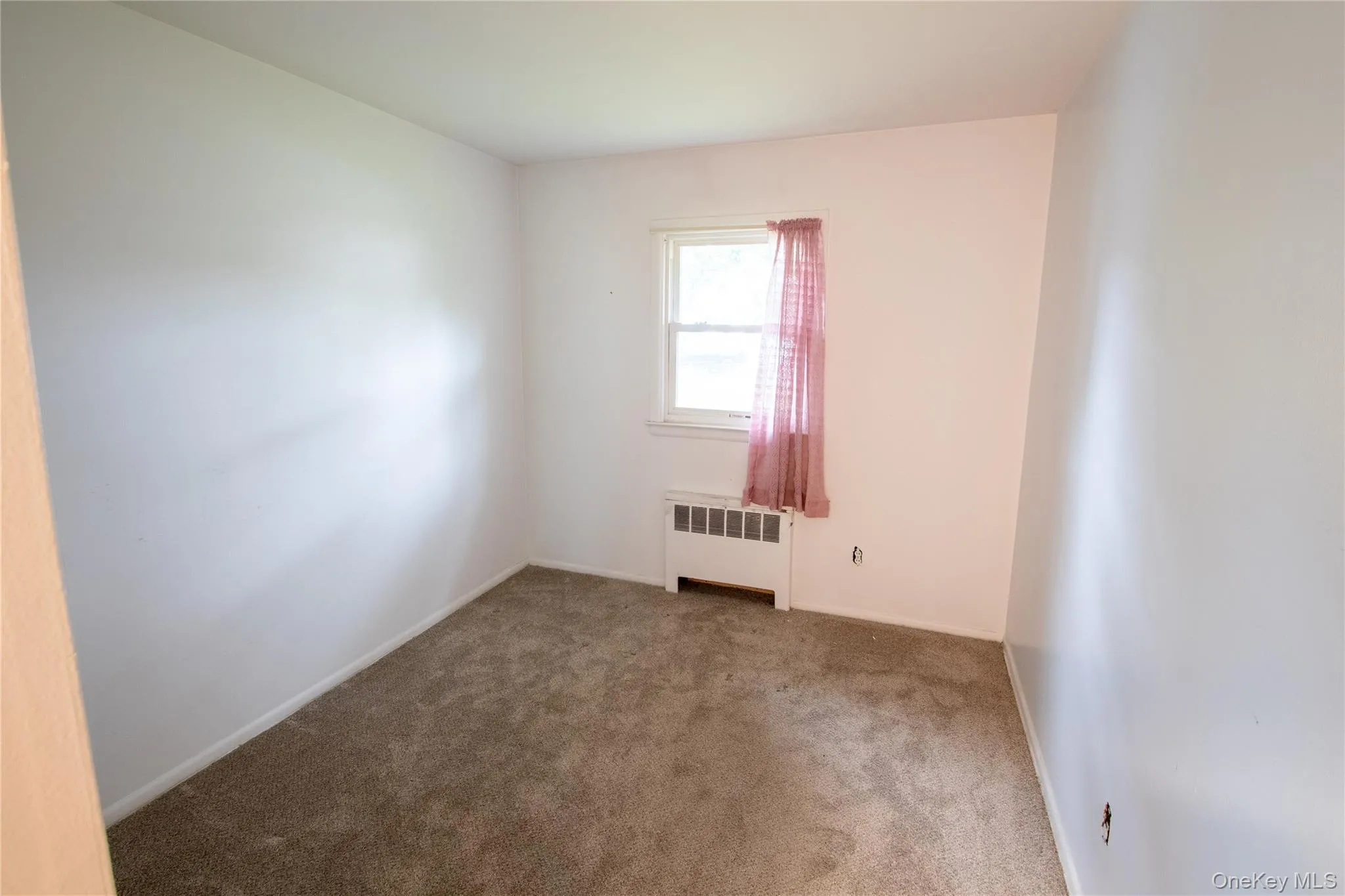 White-painted interior room with brown carpet flooring, a single window, and a baseboard heating unit White-painted interior room with brown carpet flooring, a single window, and a baseboard heating unit